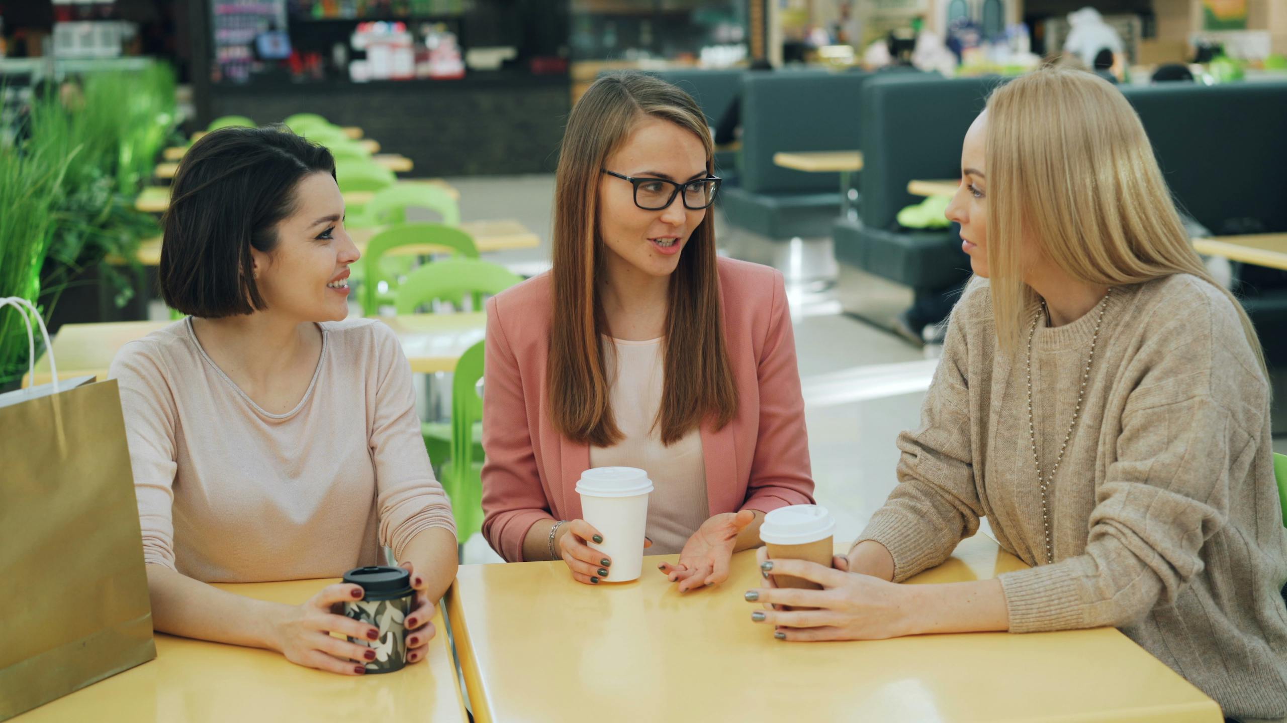 Casual conversation among friends in a modern mall cafe setting.