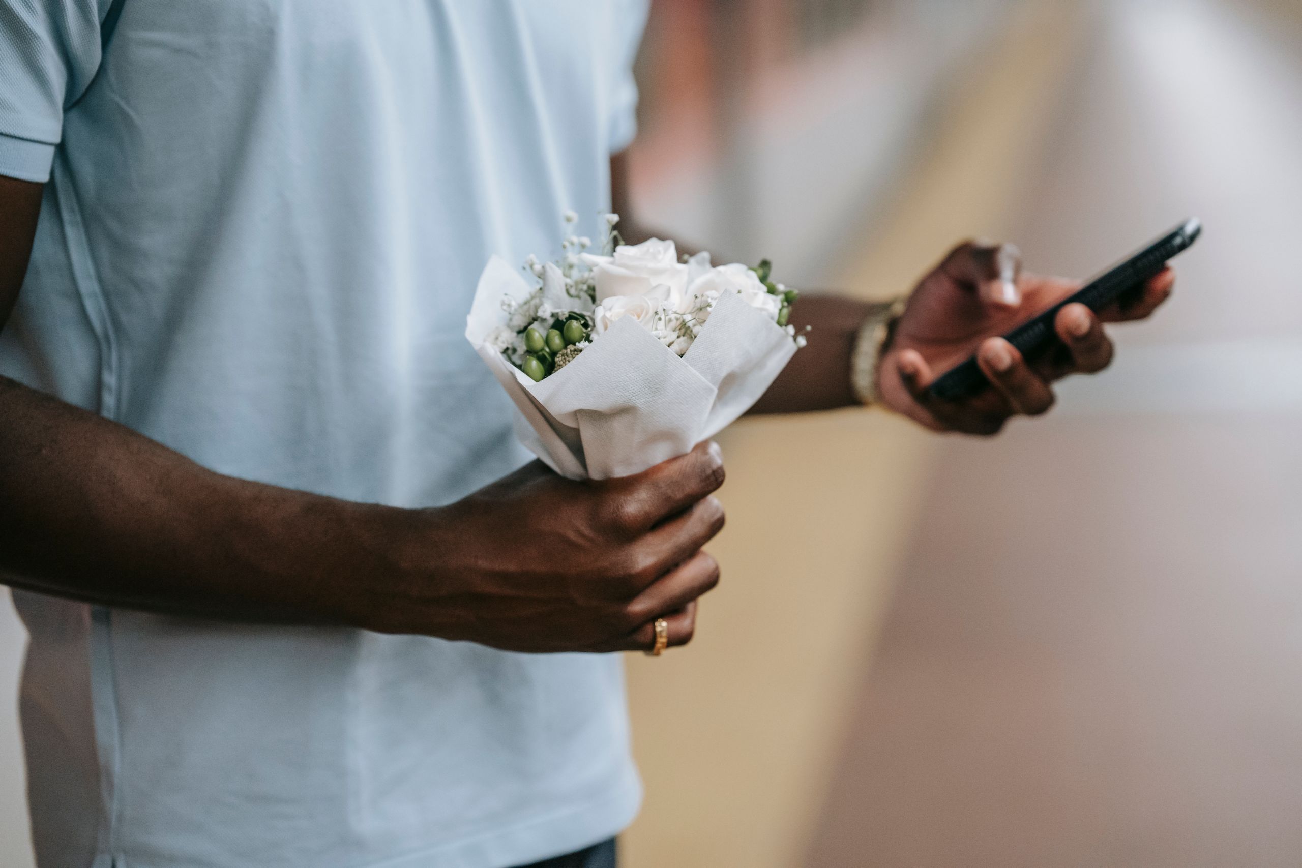 Casual shot of a man holding a small bouquet and smartphone, emphasizing a modern lifestyle.