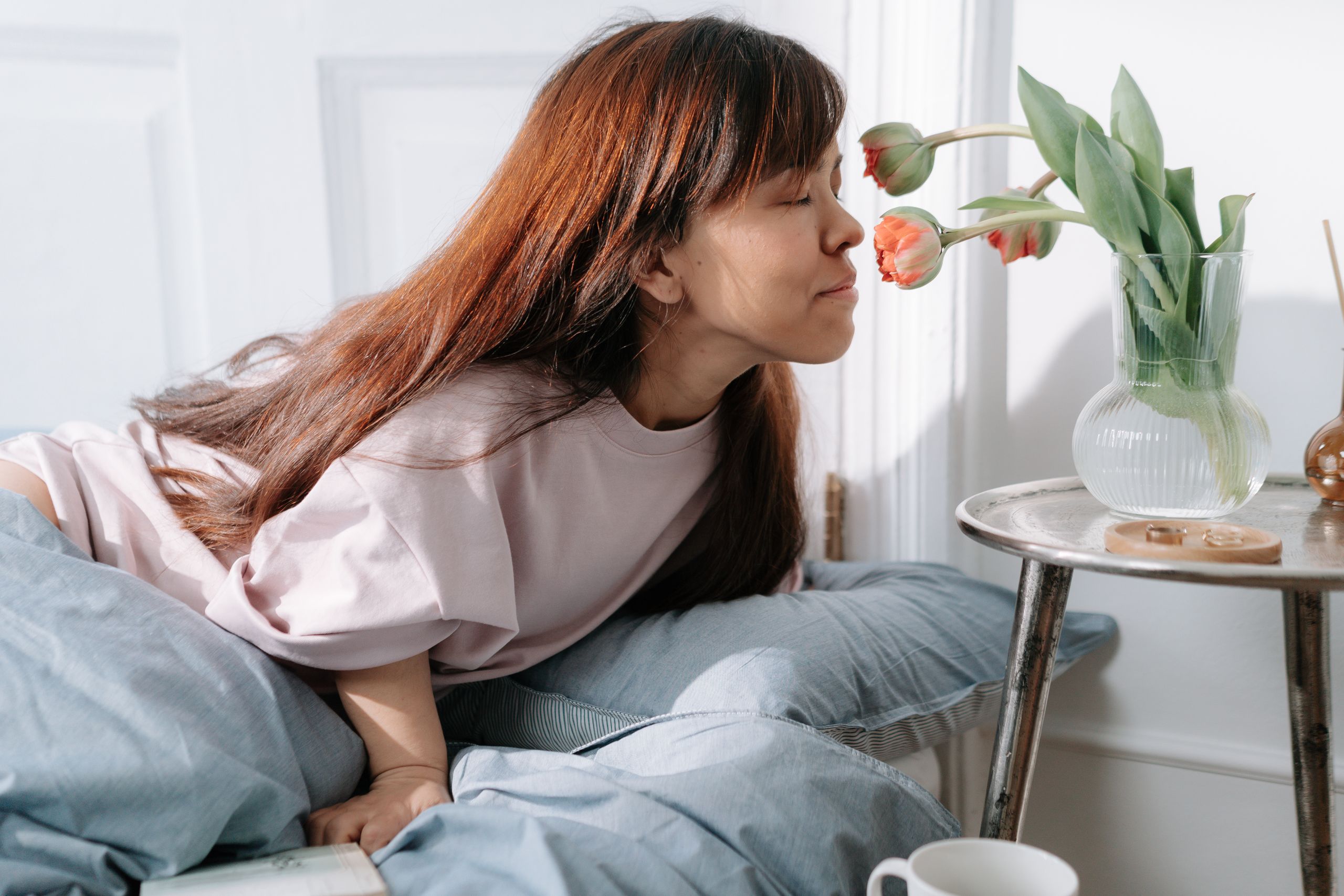 Caucasian woman with long brown hair enjoying tulips in a cozy bedroom.