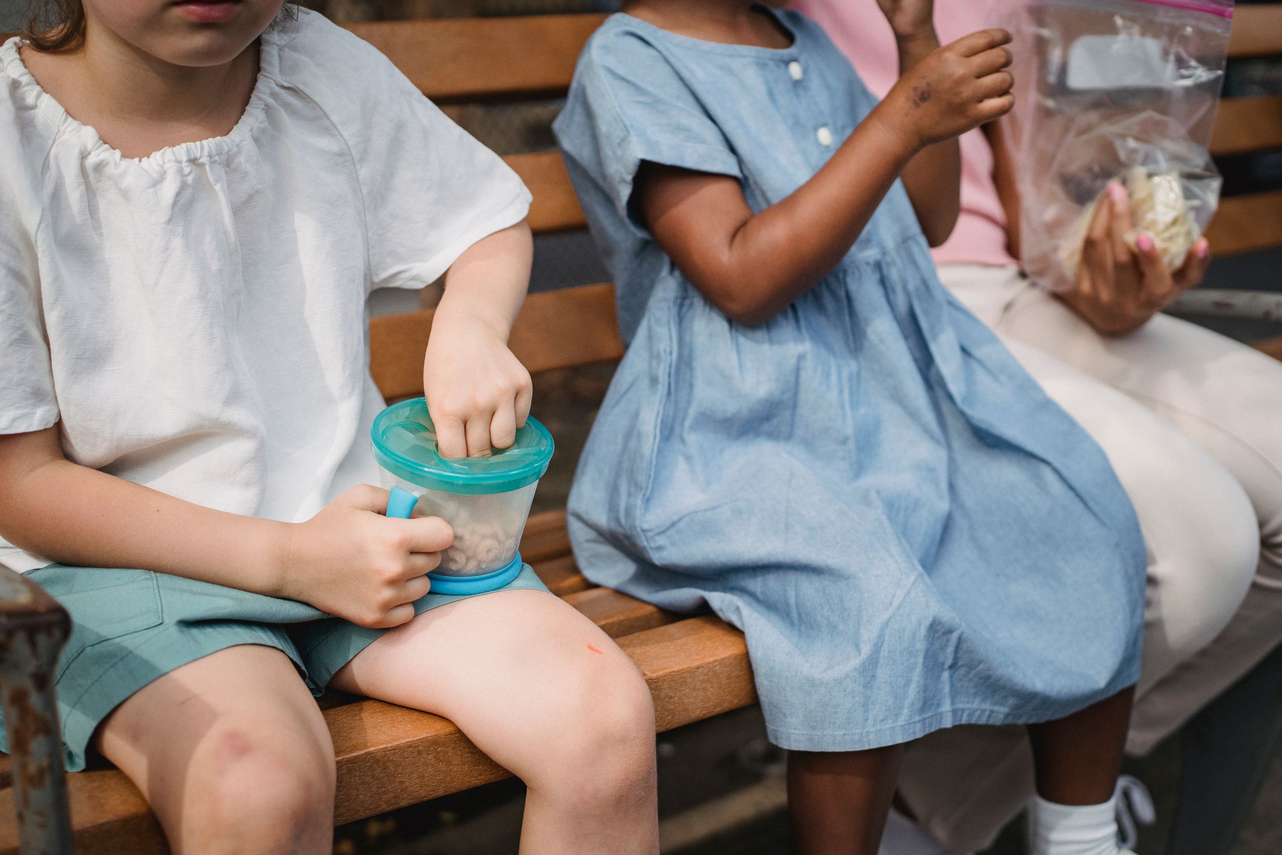 Children sitting together on a wooden bench, enjoying healthy snacks outdoors.