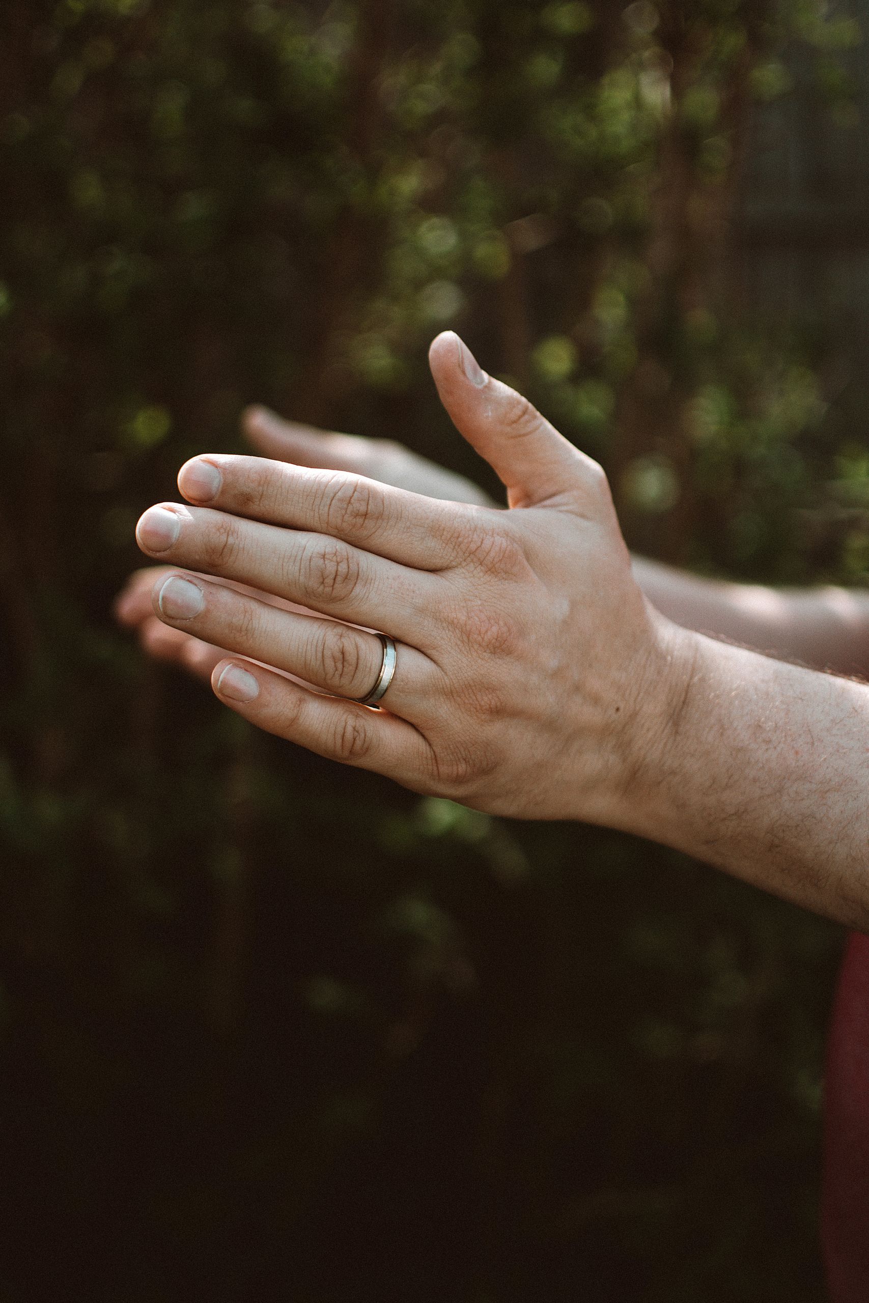 Close-up image of hands clapping outdoors with a focus on a wedding ring and natural light.