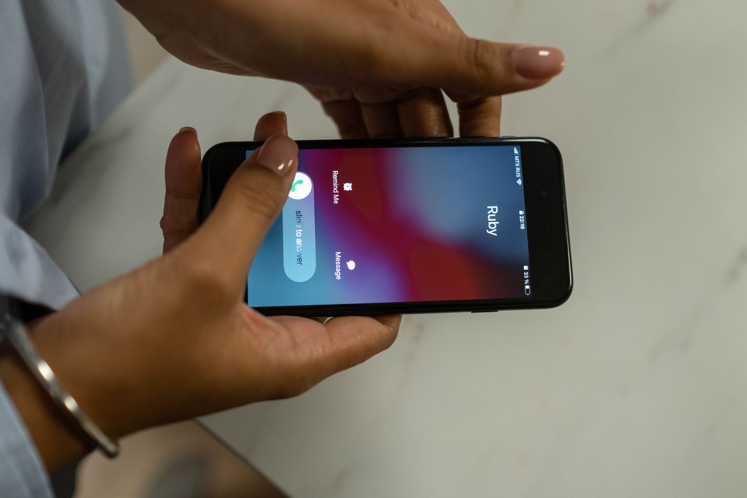 Close-up image of hands holding a smartphone receiving a call from Ruby on a marble surface.