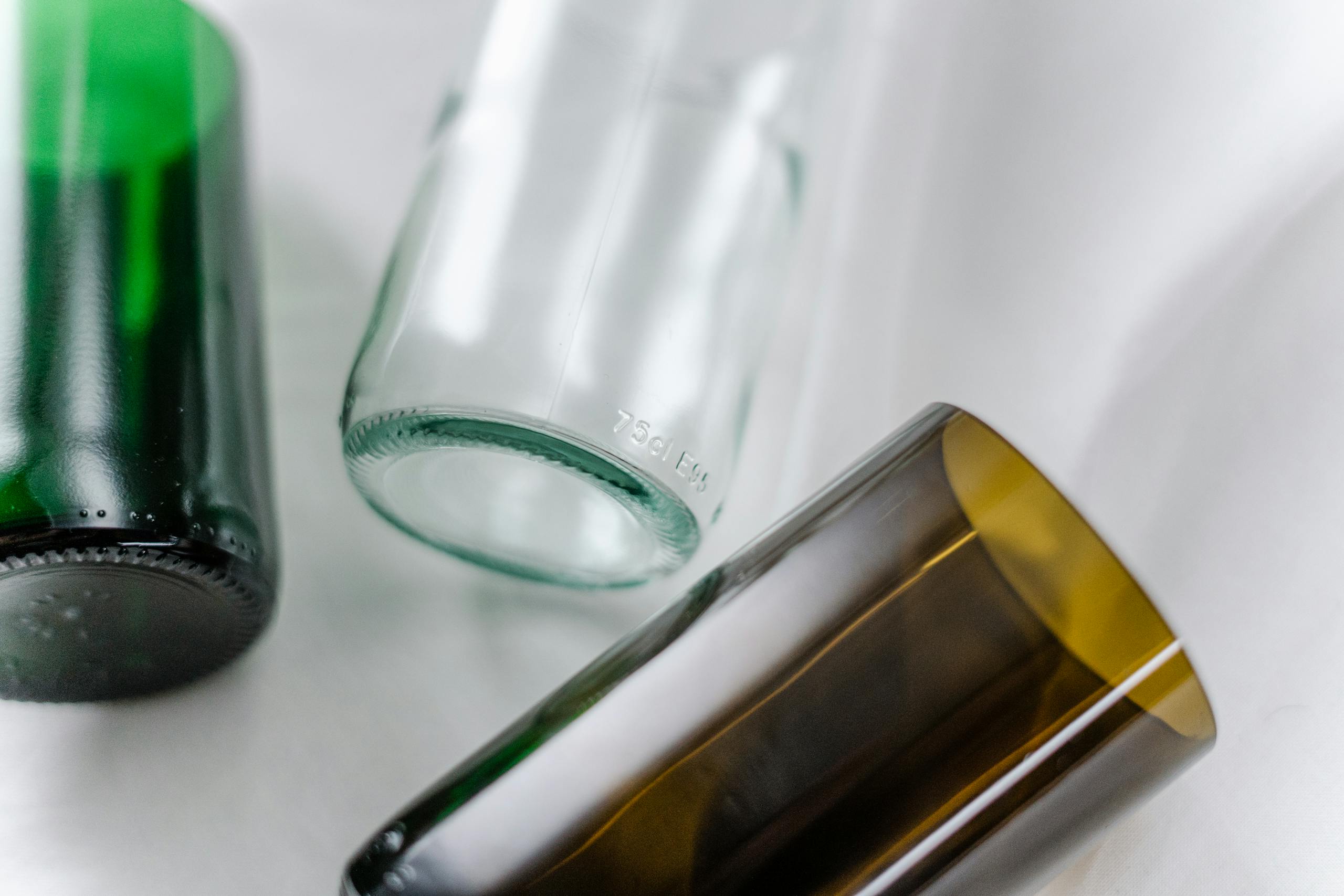 Close-up image showing three recycled glass bottles in green, clear, and brown hues on a white surface.