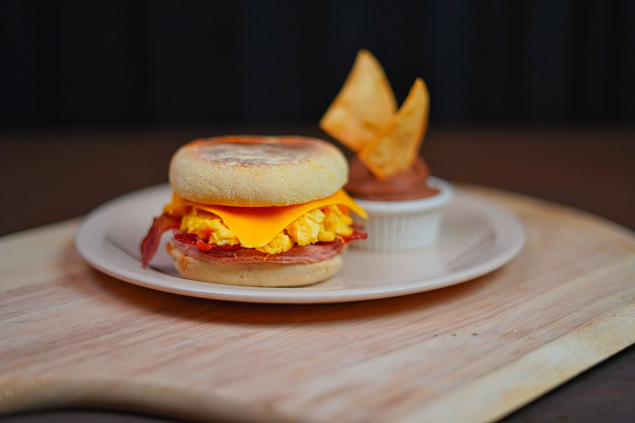 Close-up of a breakfast sandwich with eggs, cheese, and bacon on a ceramic plate.
