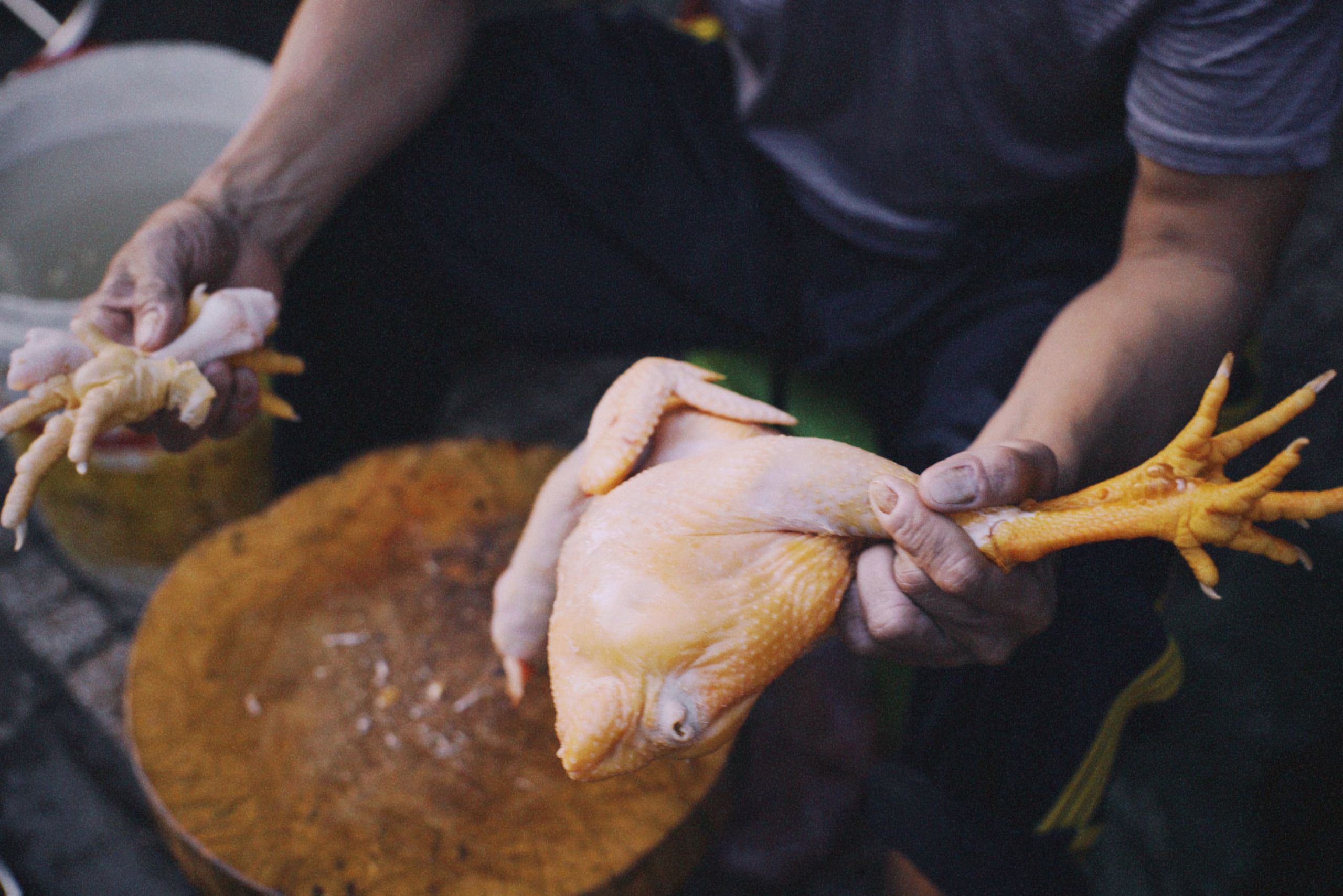 Close-up of a butcher holding a raw chicken for preparation on a wooden board.