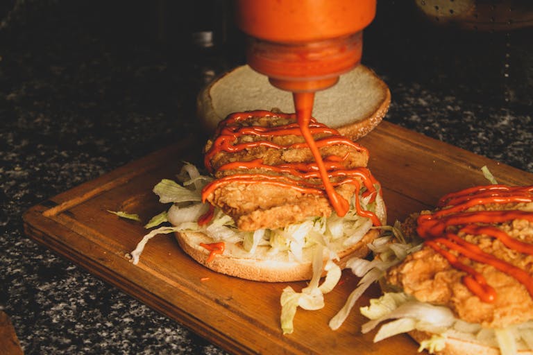 Close-up of a chicken sandwich being prepared with sauce on a wooden board.
