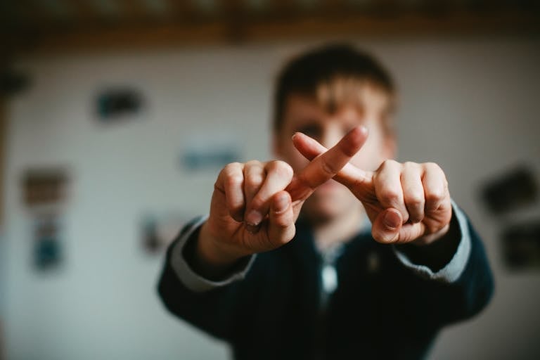 Close-up of a child crossing fingers in an indoor setting with a blurred background.