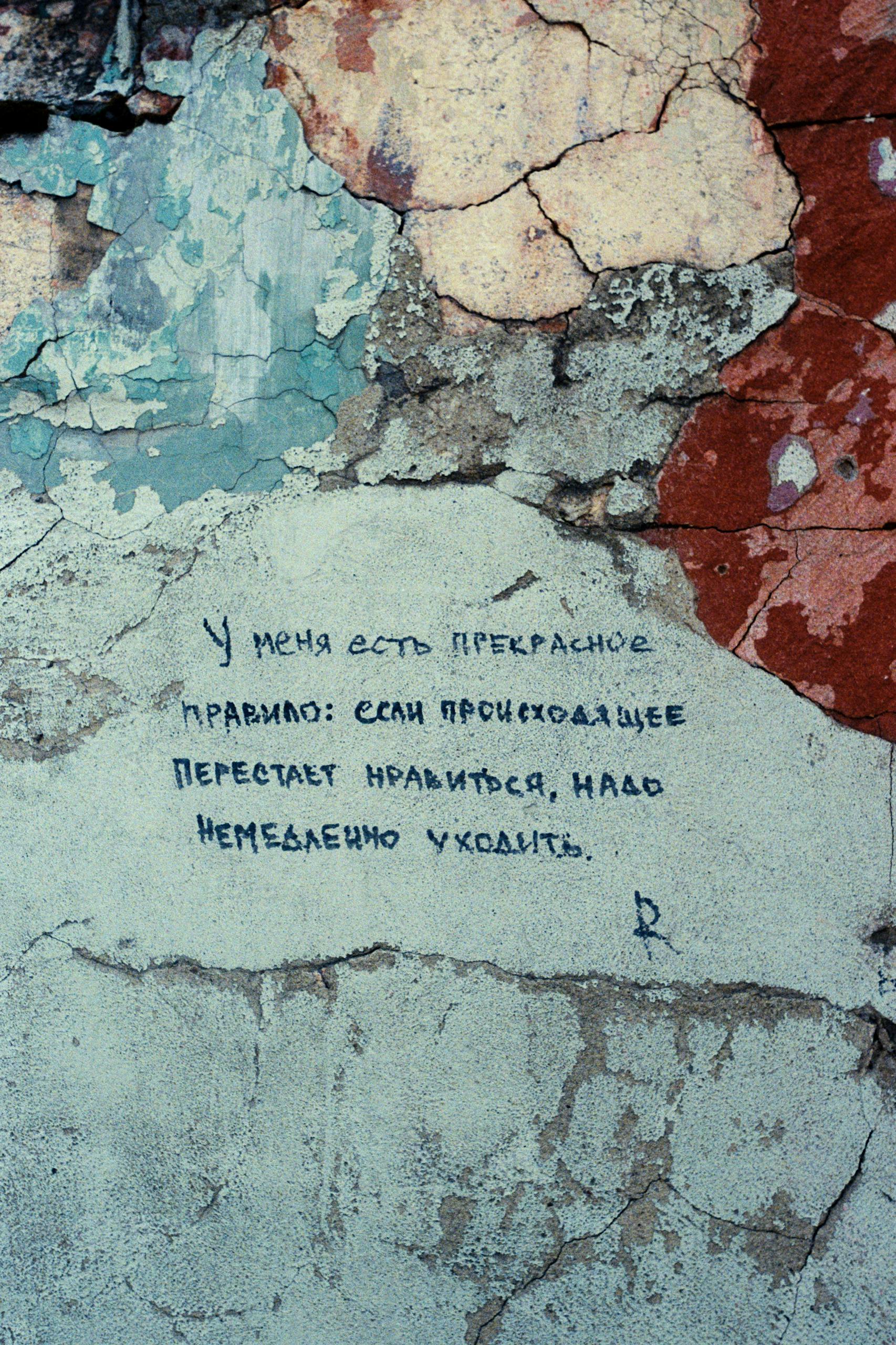 Close-up of a cracked, weathered wall with Russian handwritten text.