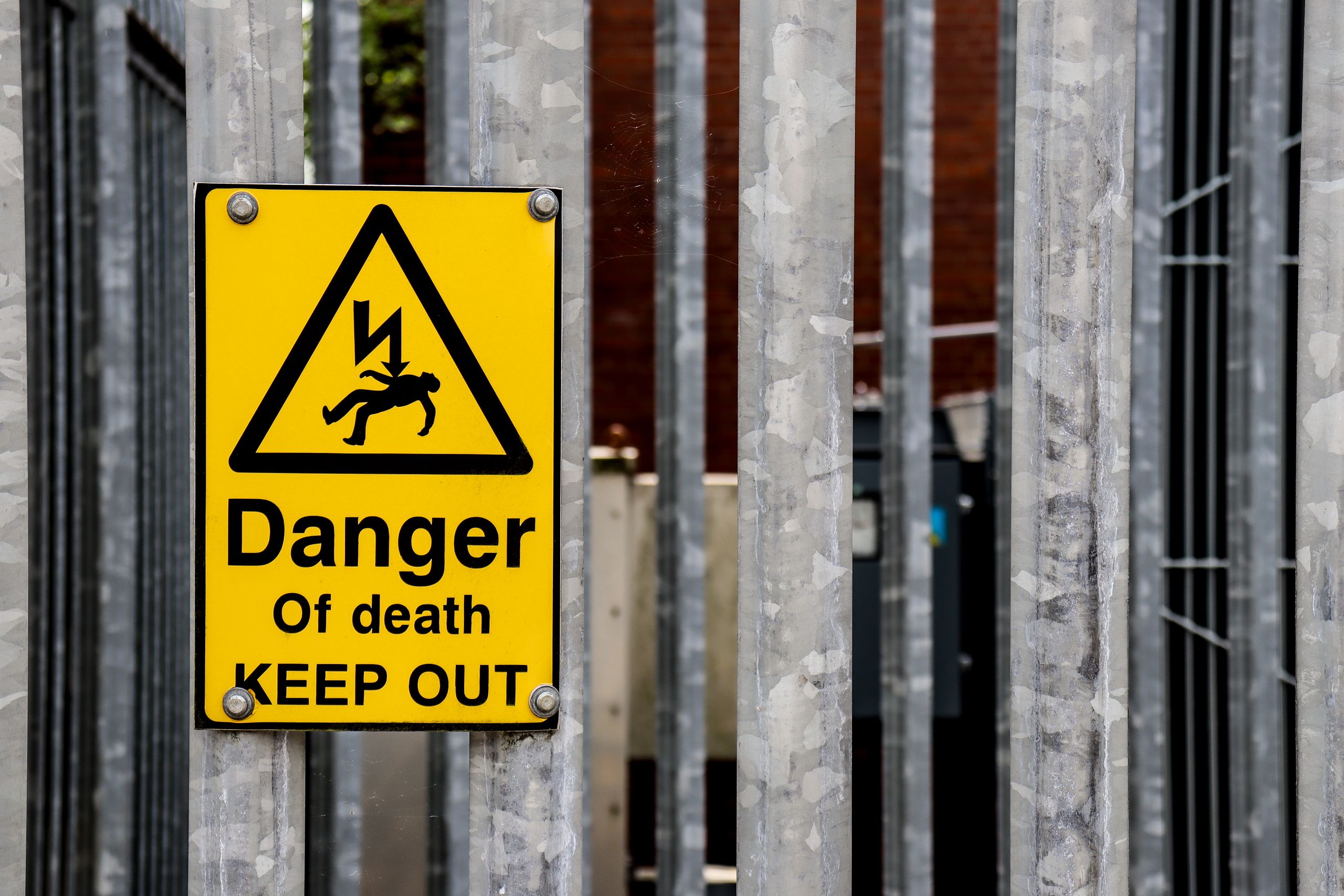 Close-up of a danger of death warning sign on a metal fence outdoors.