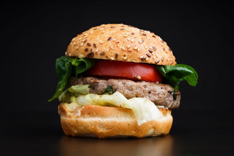 Close-up of a delicious burger with lettuce, tomato, and sesame seed bun on black background.