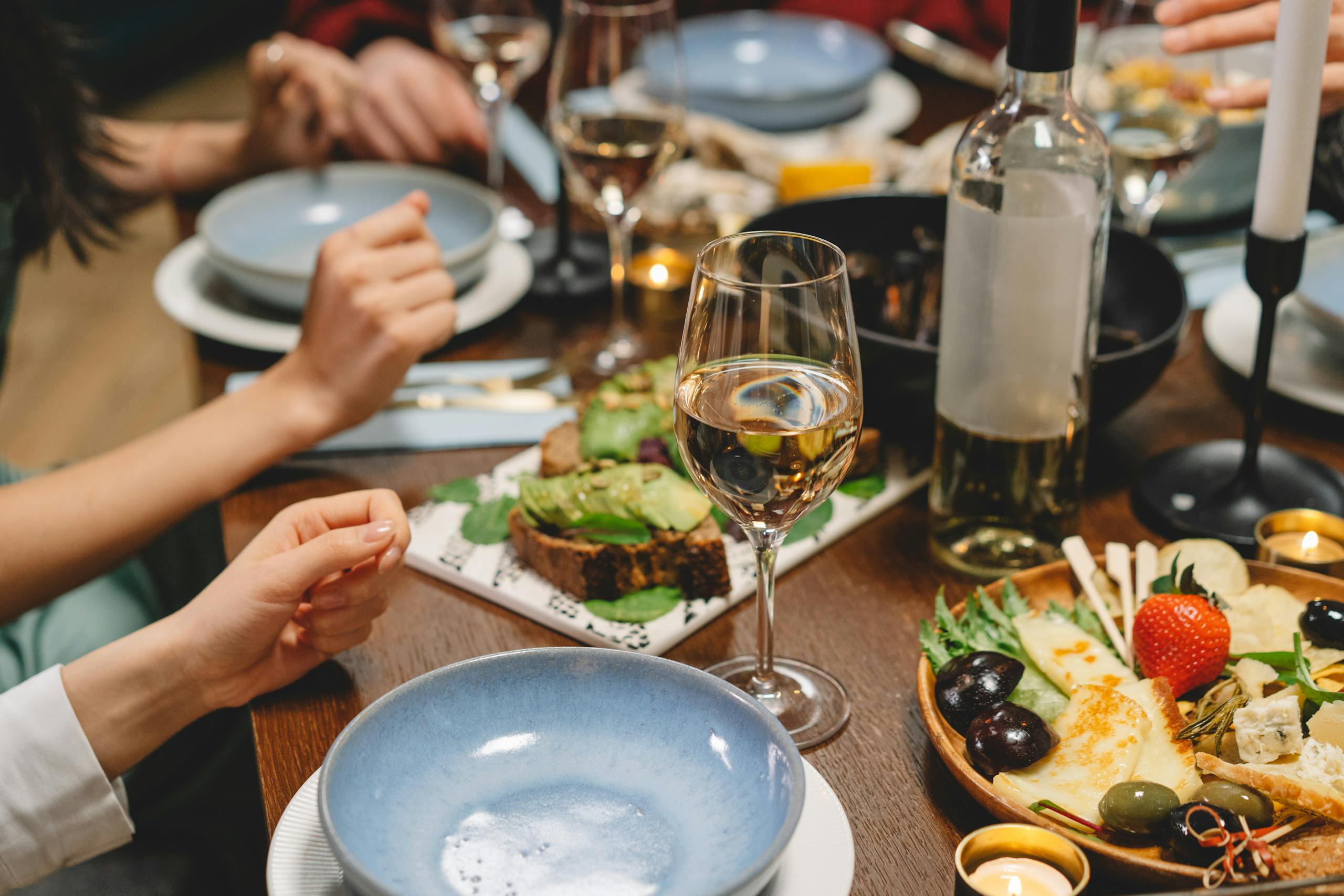 Close-up of a dinner table with wine, appetizers, and people enjoying a meal in a cozy indoor setting.