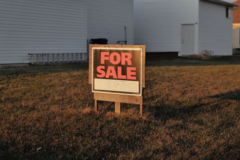 Close-up of a 'For Sale' sign in a suburban yard, indicating a property for sale.