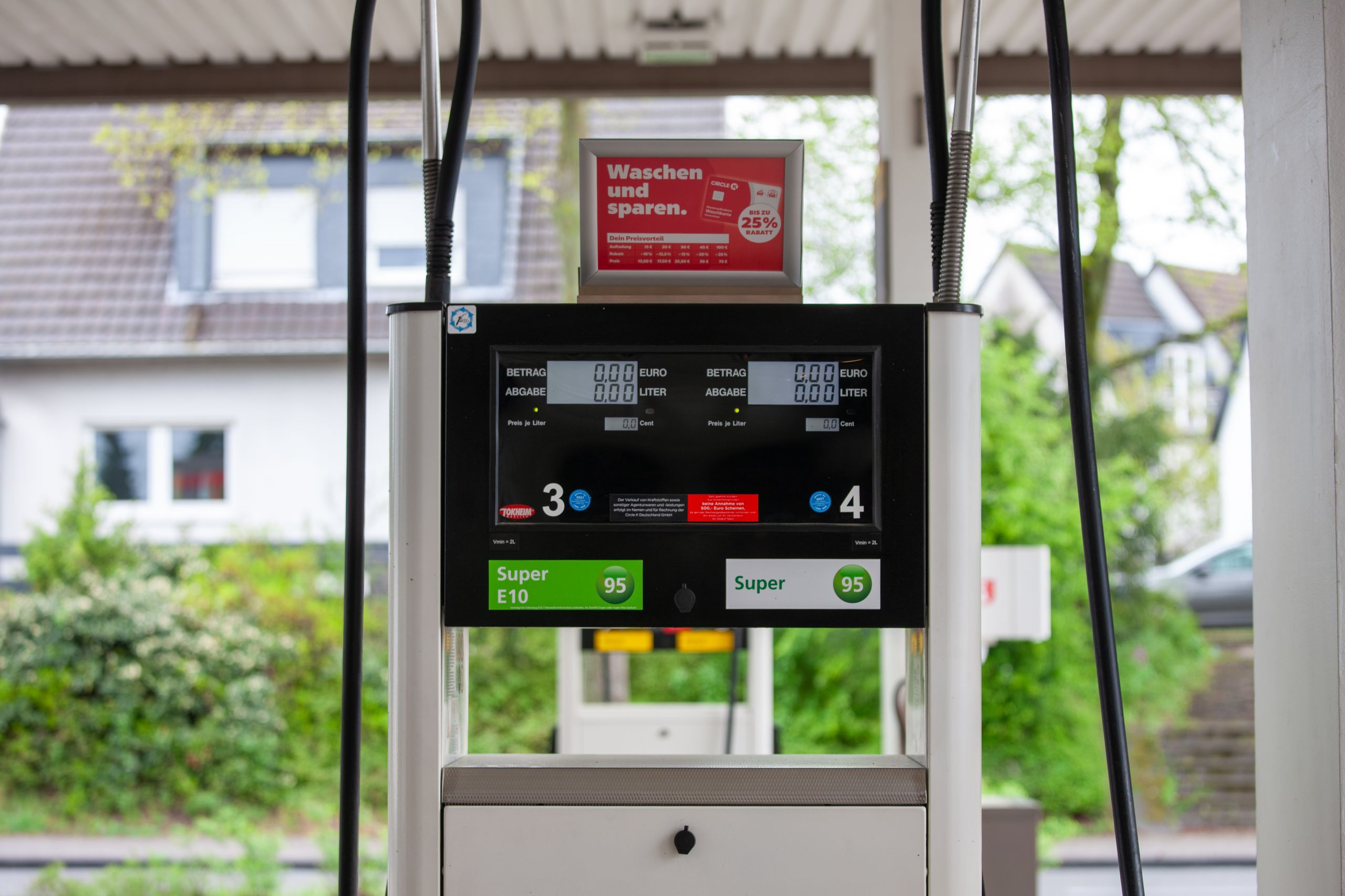 Close-up of a gas pump at a station in Bergisch Gladbach, Germany, with surrounding houses visible.