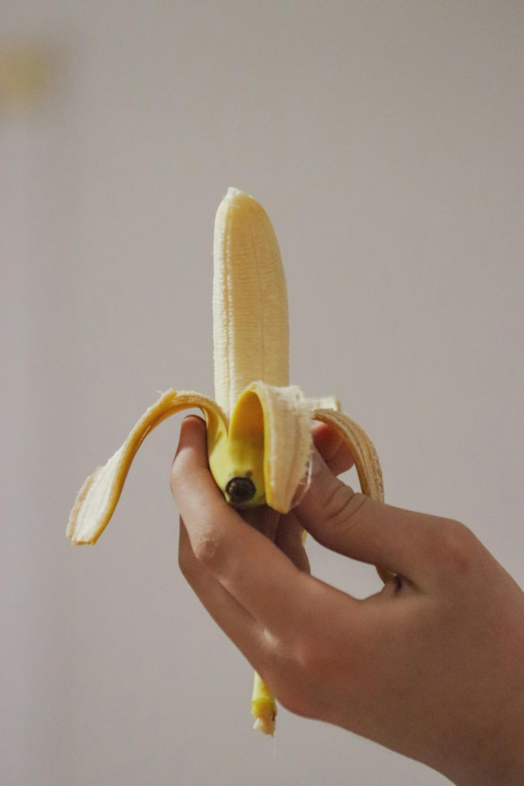 Close-up of a hand holding a partially peeled banana, highlighting fruit freshness.