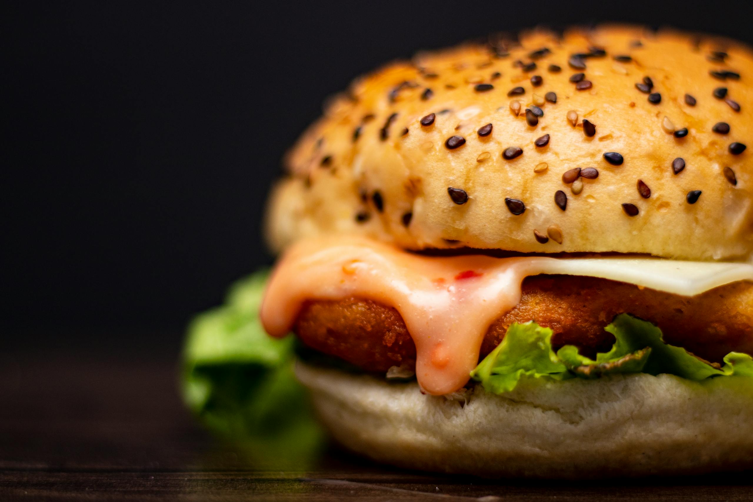 Close-up of a mouthwatering chicken burger with lettuce and cheese on a black background.