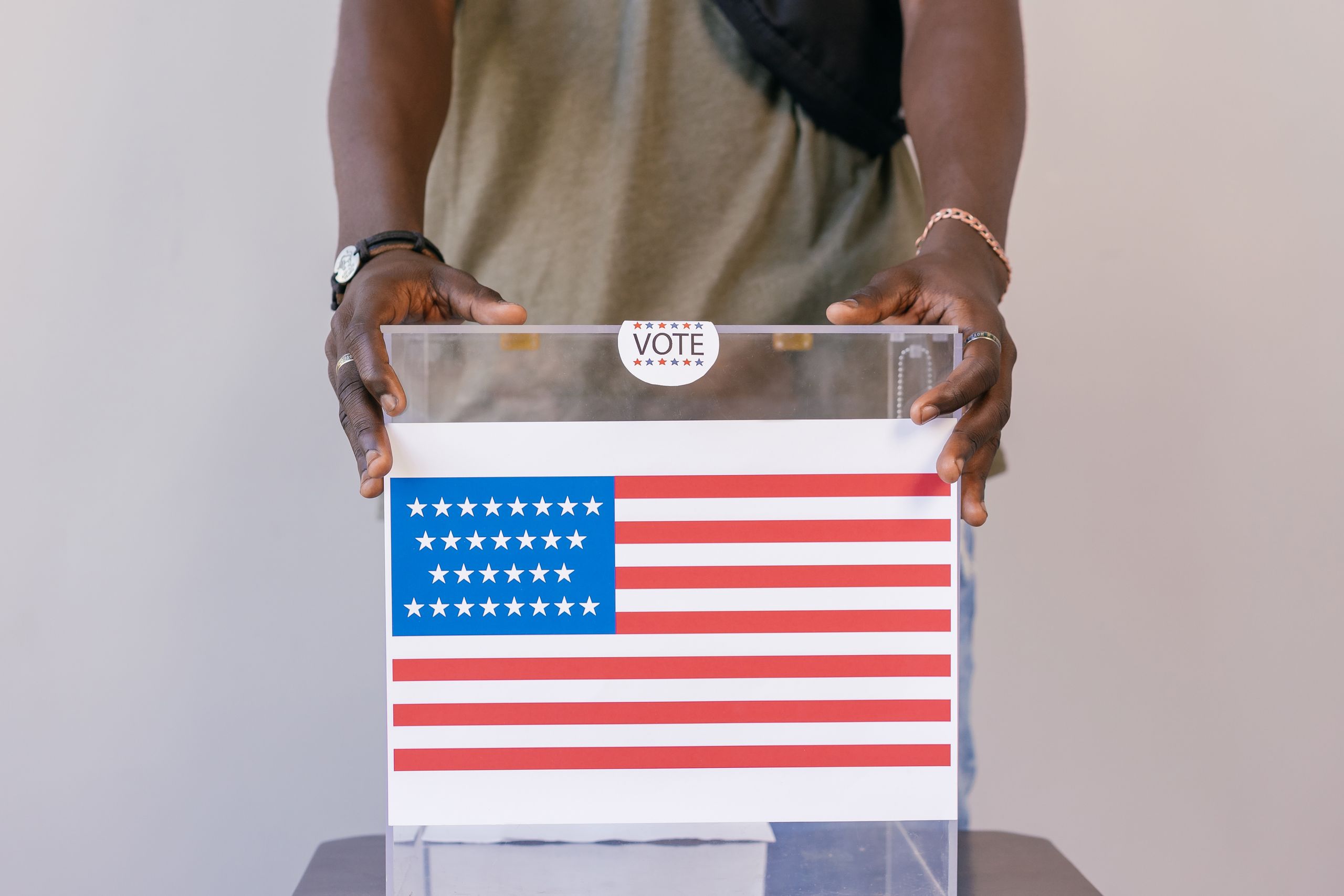 Close-up of a person placing a vote in a transparent ballot box with an American flag print.