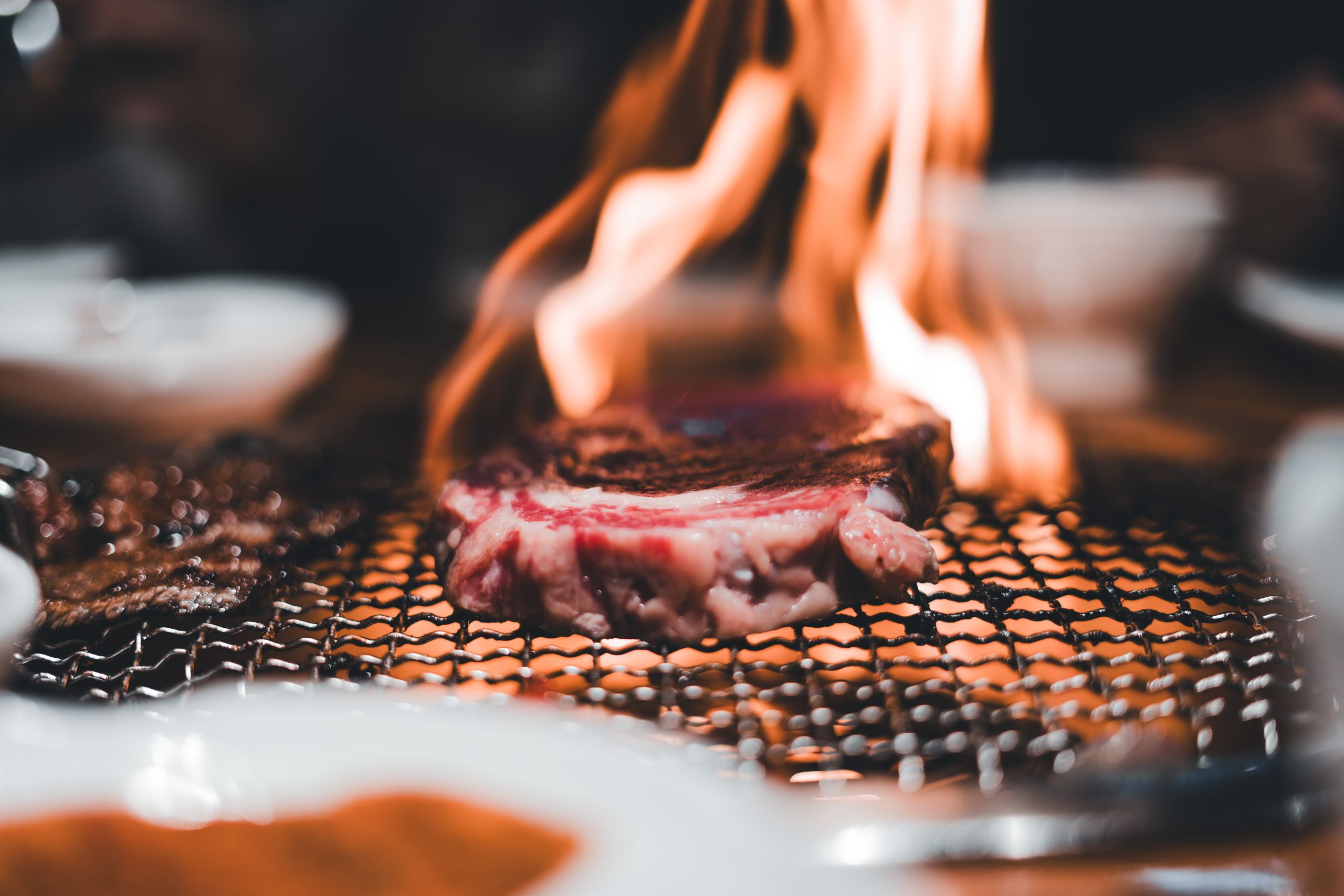 Close-up of a steak being grilled on a charcoal BBQ with visible flames, creating an appetizing view.