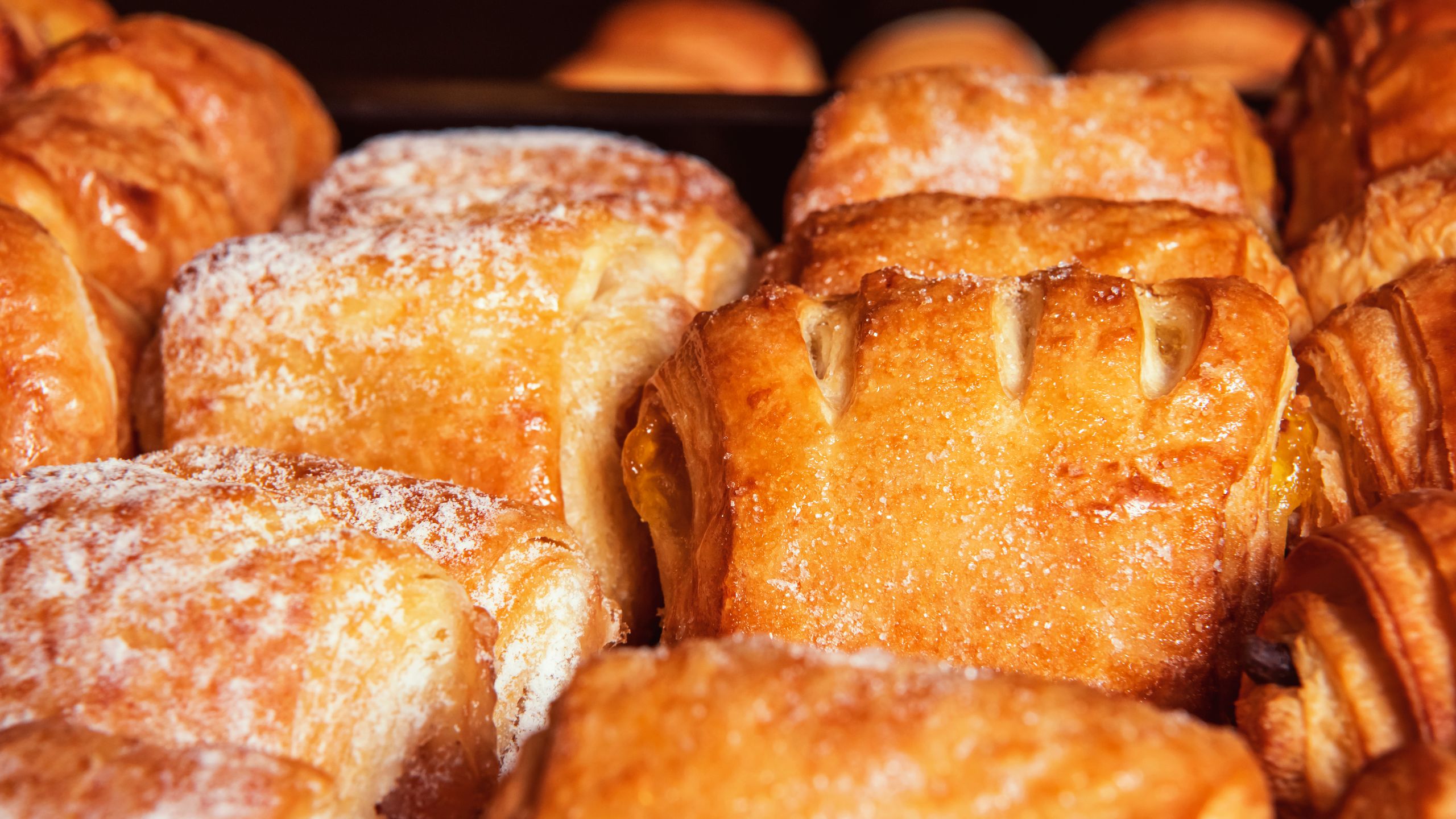 Close-up of a variety of freshly baked pastries dusted with powdered sugar, showcasing flaky texture.