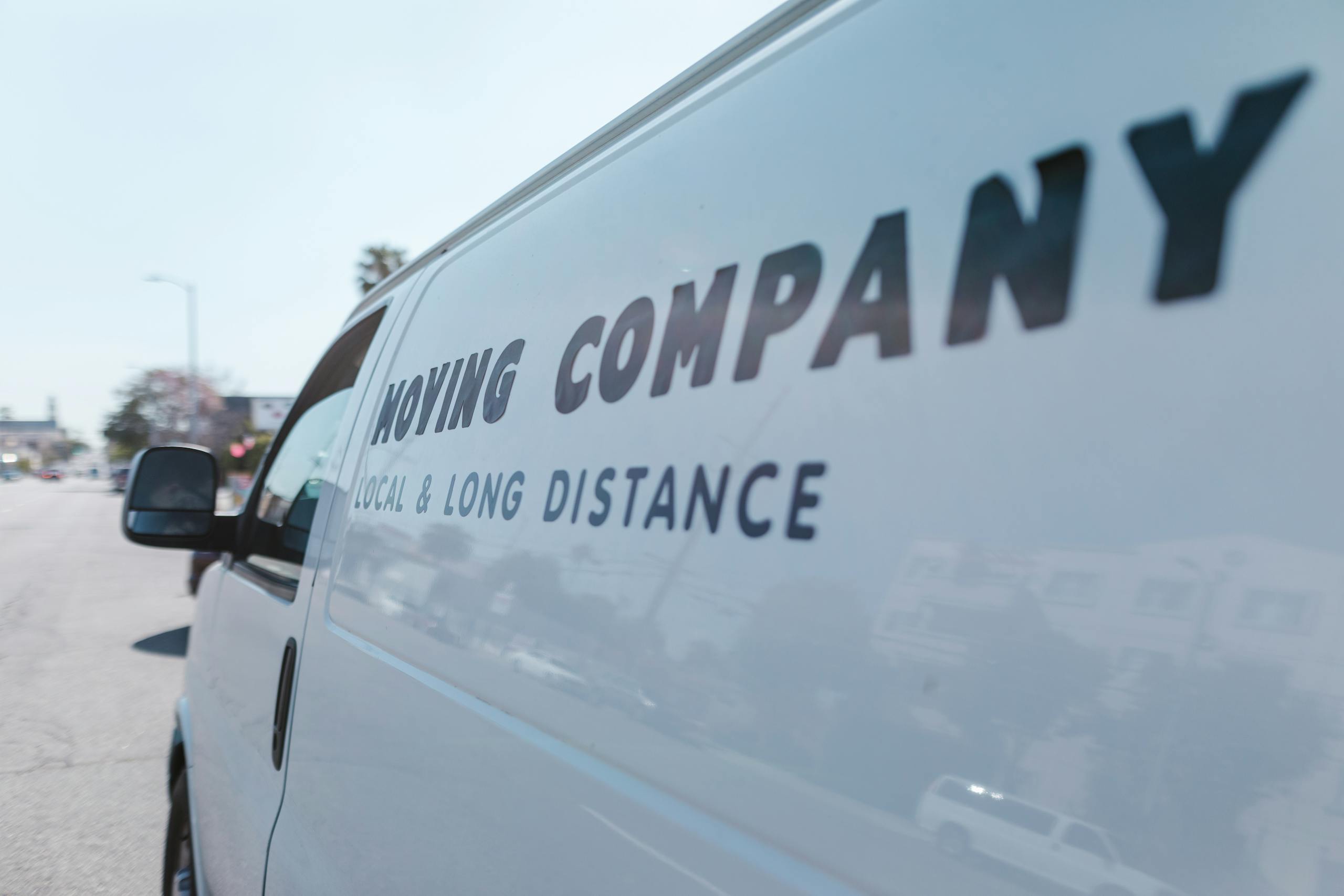 Close-up of a white moving company van with text on a sunny day street.
