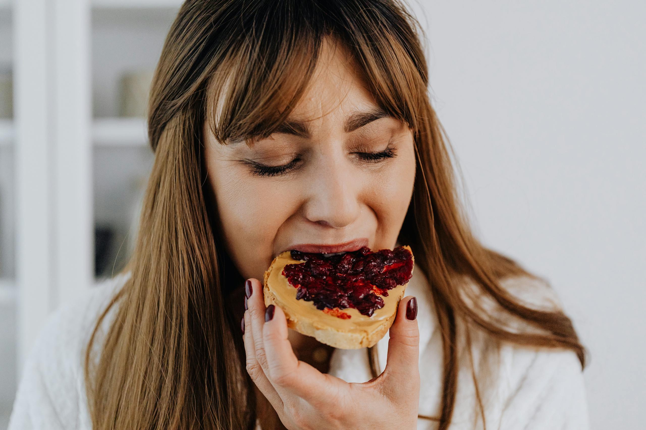Close-up of a woman savoring a delicious peanut butter and jelly sandwich indoors.