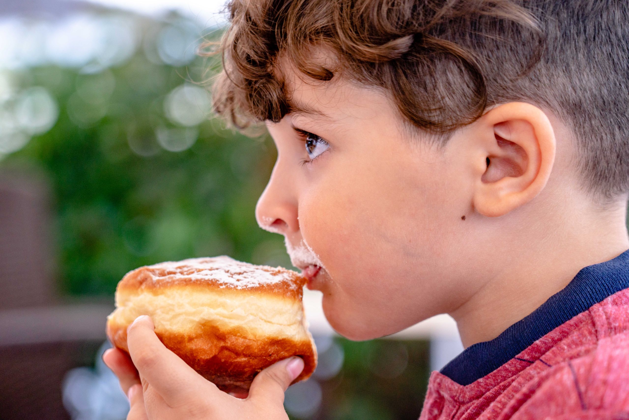 Close-up of a young child savoring a doughnut with powdered sugar outdoors.