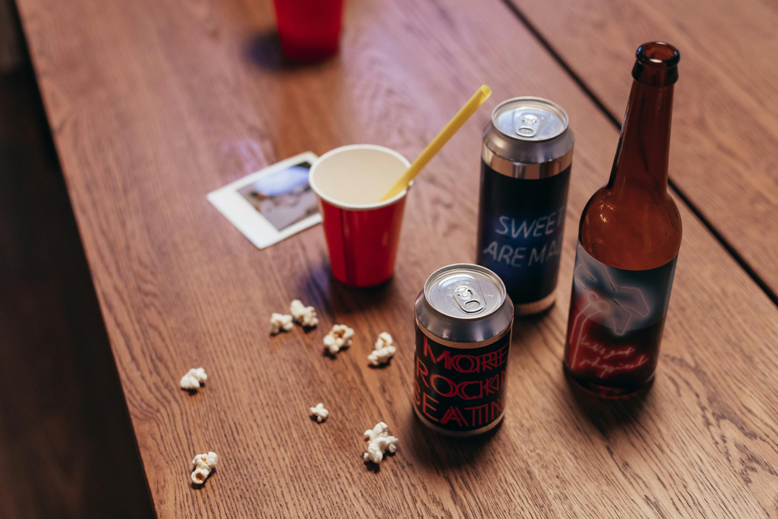 Close-up of assorted drinks and snacks on a wooden table, evoking a casual gathering vibe.