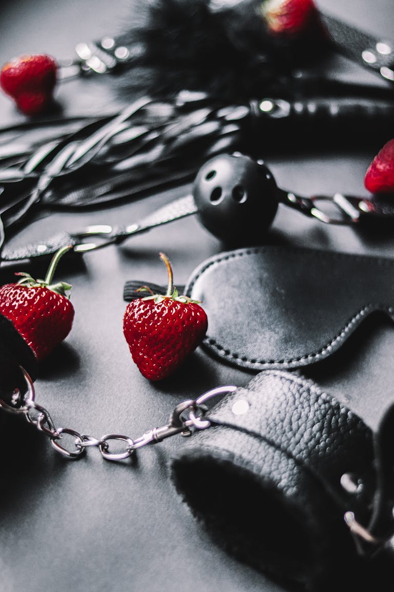 Close-up of black leather BDSM gear with strawberries, creating a sensual atmosphere.