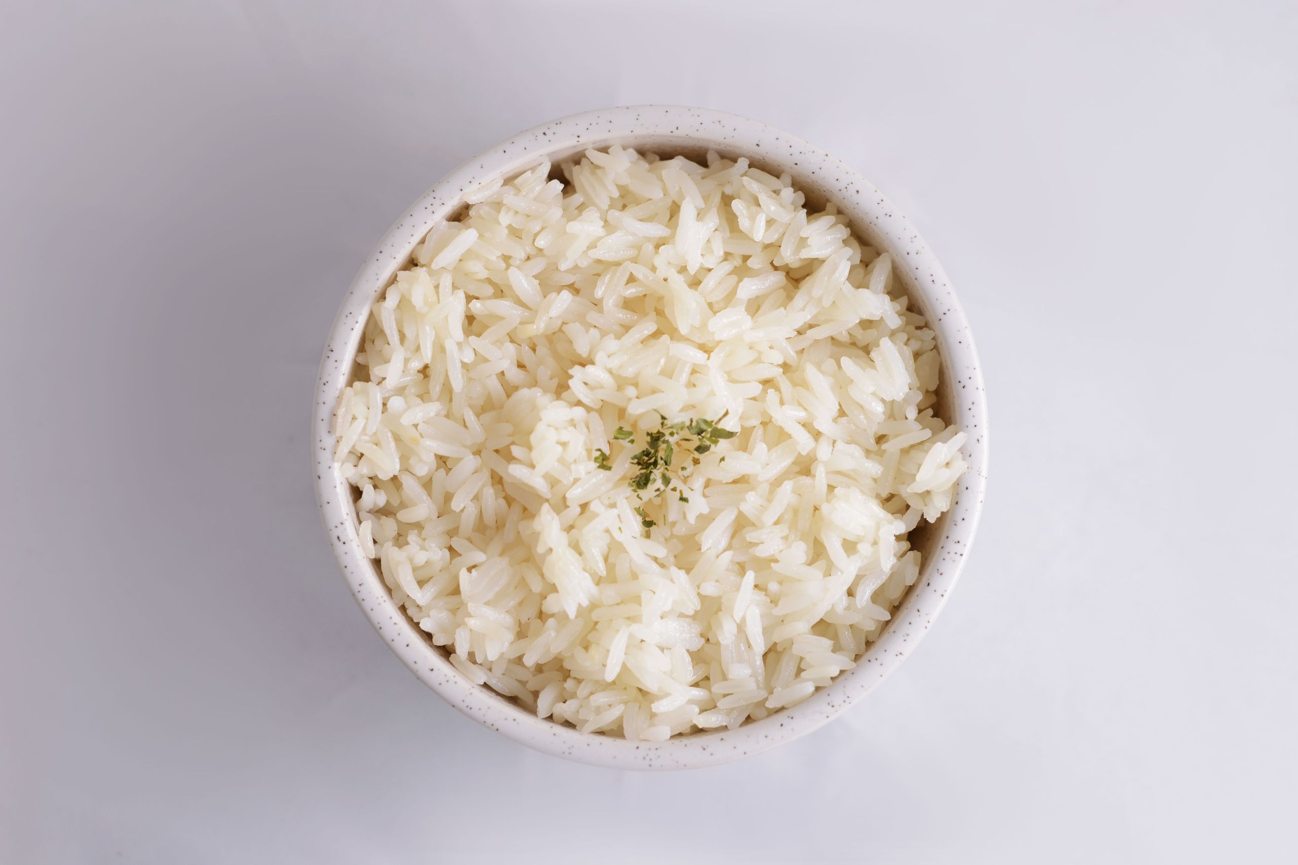 Close-up of cooked white rice in a bowl, garnished with herbs, in a minimalist setup.
