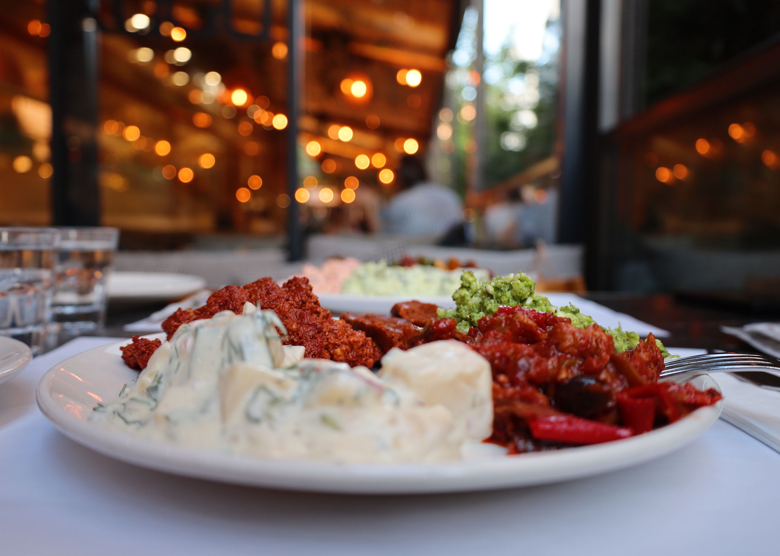 Close-up of diverse Mediterranean tapas on a white plate at a cozy outdoor restaurant.