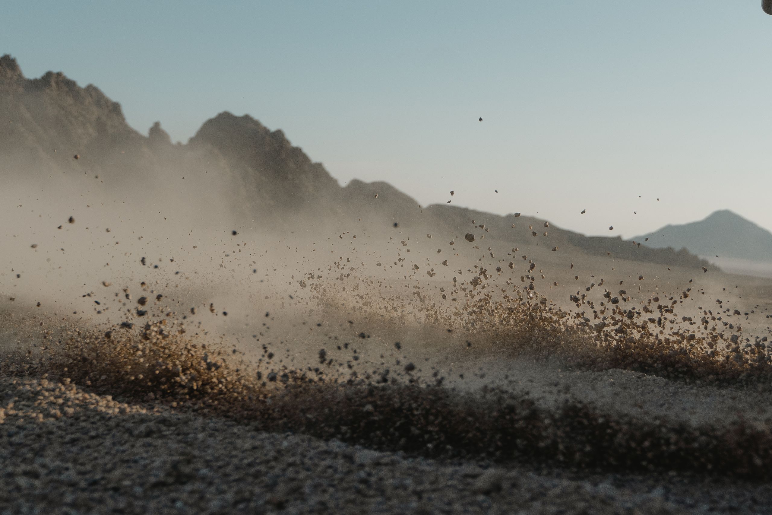Close-up of dust cloud forming in rocky desert landscape with mountain backdrop.