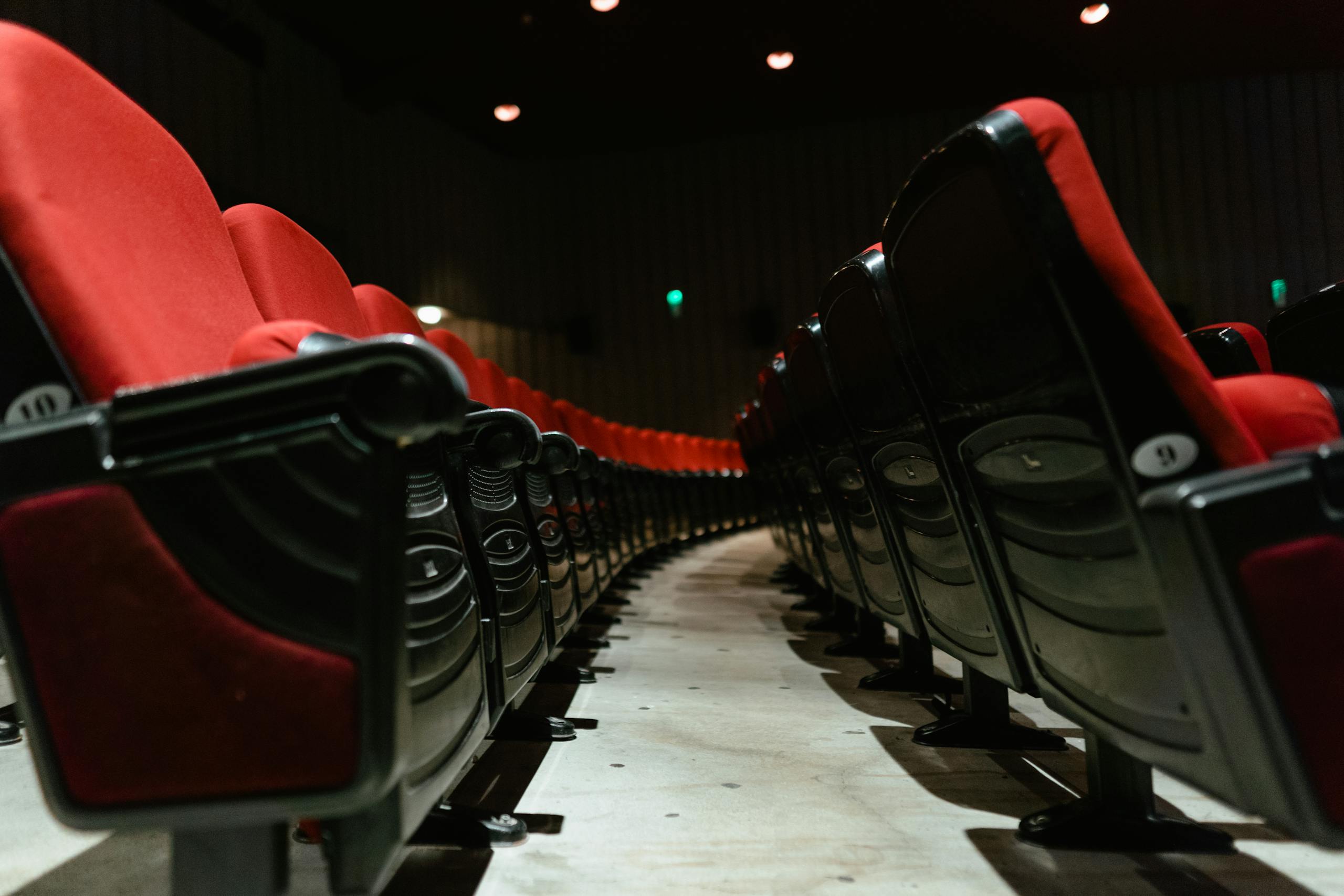 Close-up of empty red upholstered seats in a dimly lit theater interior.