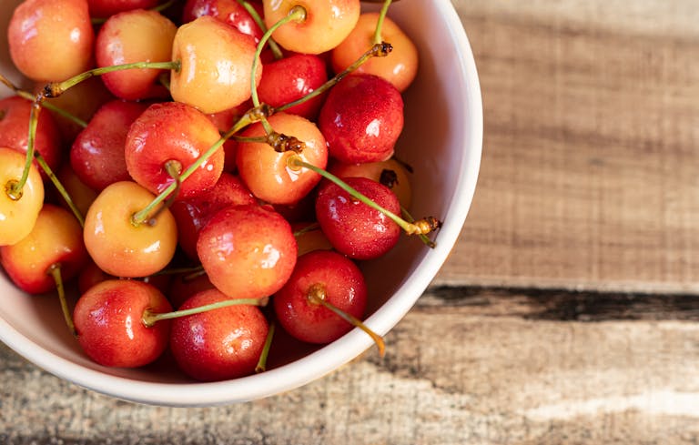 Close-up of fresh Rainier cherries in a white bowl on a wooden surface.