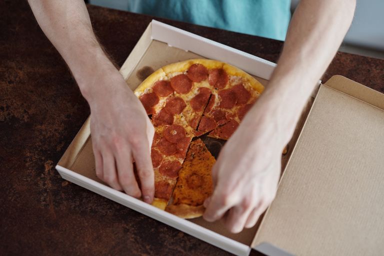 Close-up of hands taking a slice of pepperoni pizza from a cardboard box.