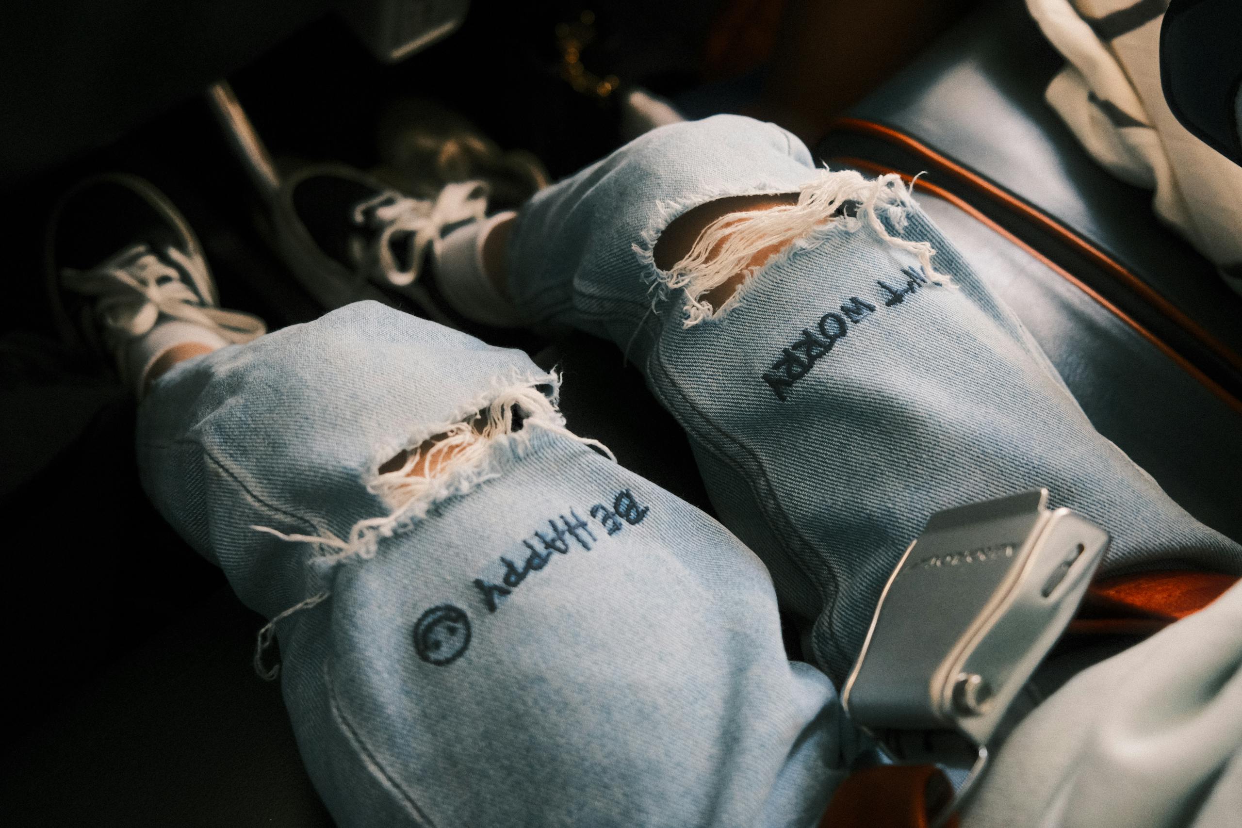 Close-up of legs in ripped jeans and sneakers, showing casual fashion style and focus on safety with seatbelt.