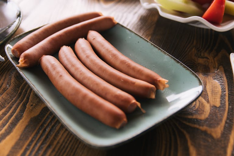Close-up of sausages on a ceramic plate on a rustic wooden table.