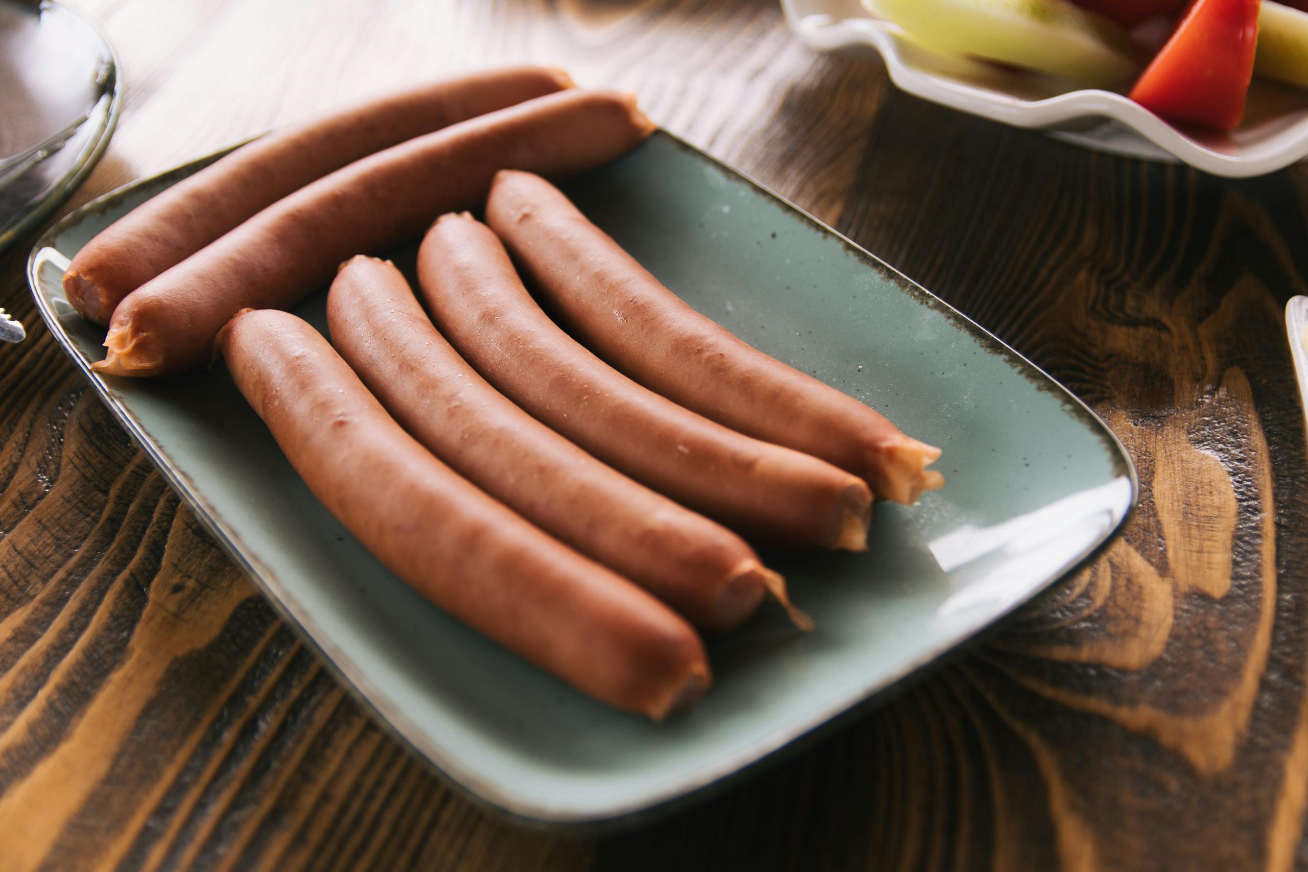 Close-up of sausages on a ceramic plate on a rustic wooden table.