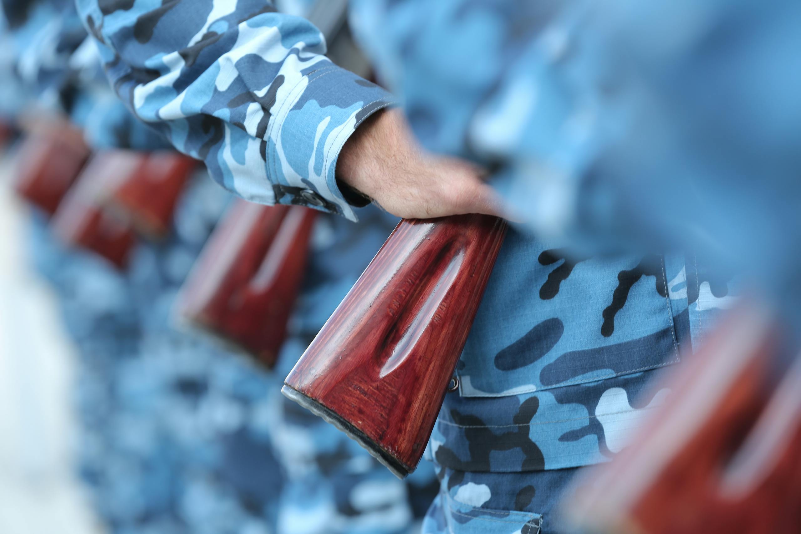 Close-up of soldiers in blue camouflage holding rifles in formation.