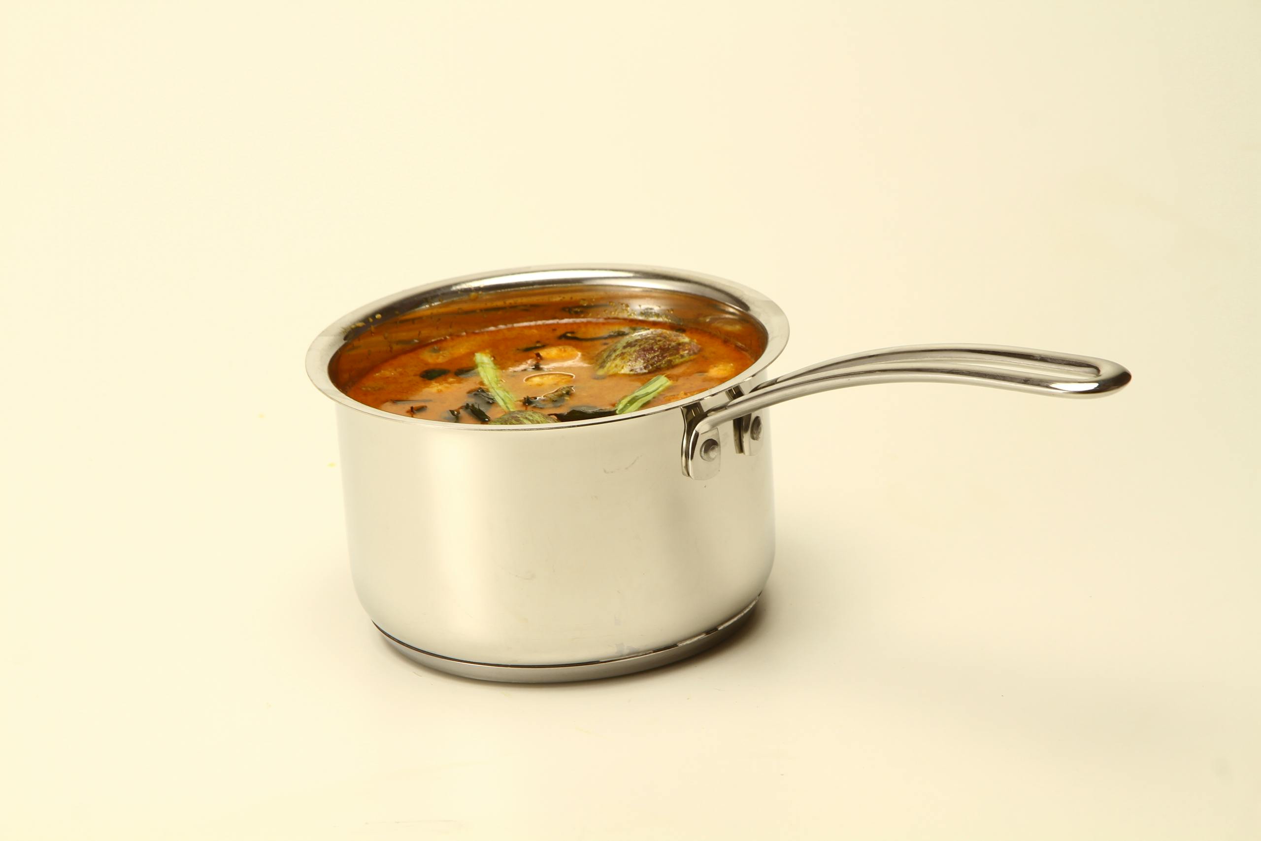 Close-up of South Indian sambar in a stainless steel pot on a white background.