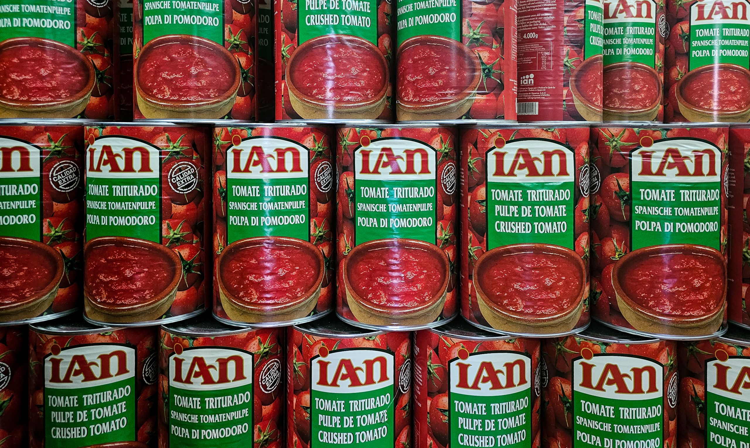 Close-up of stacked cans of crushed tomatoes in vibrant red with multilingual labels.