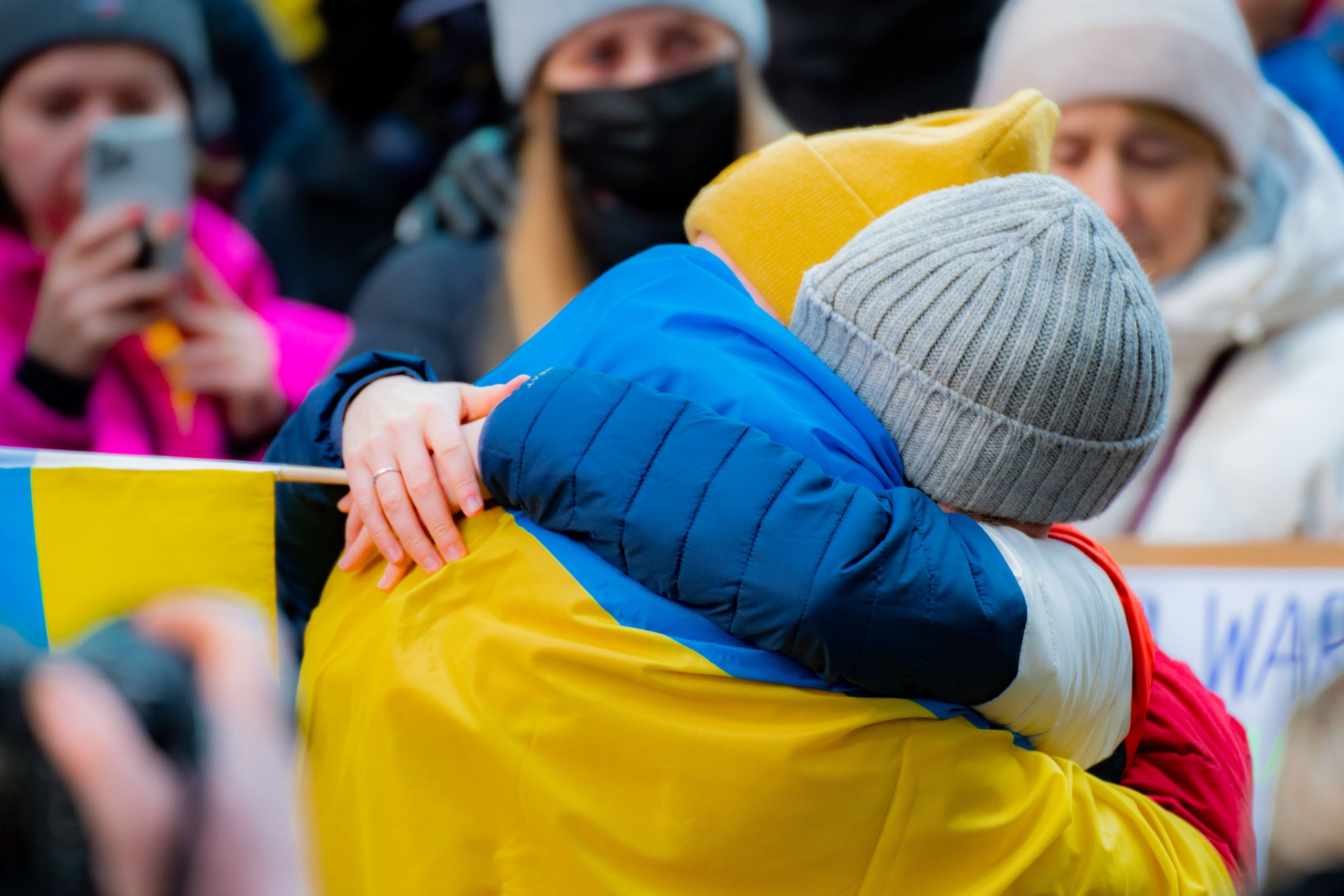 Close-up of two adults embracing at a New York protest, with people in background.