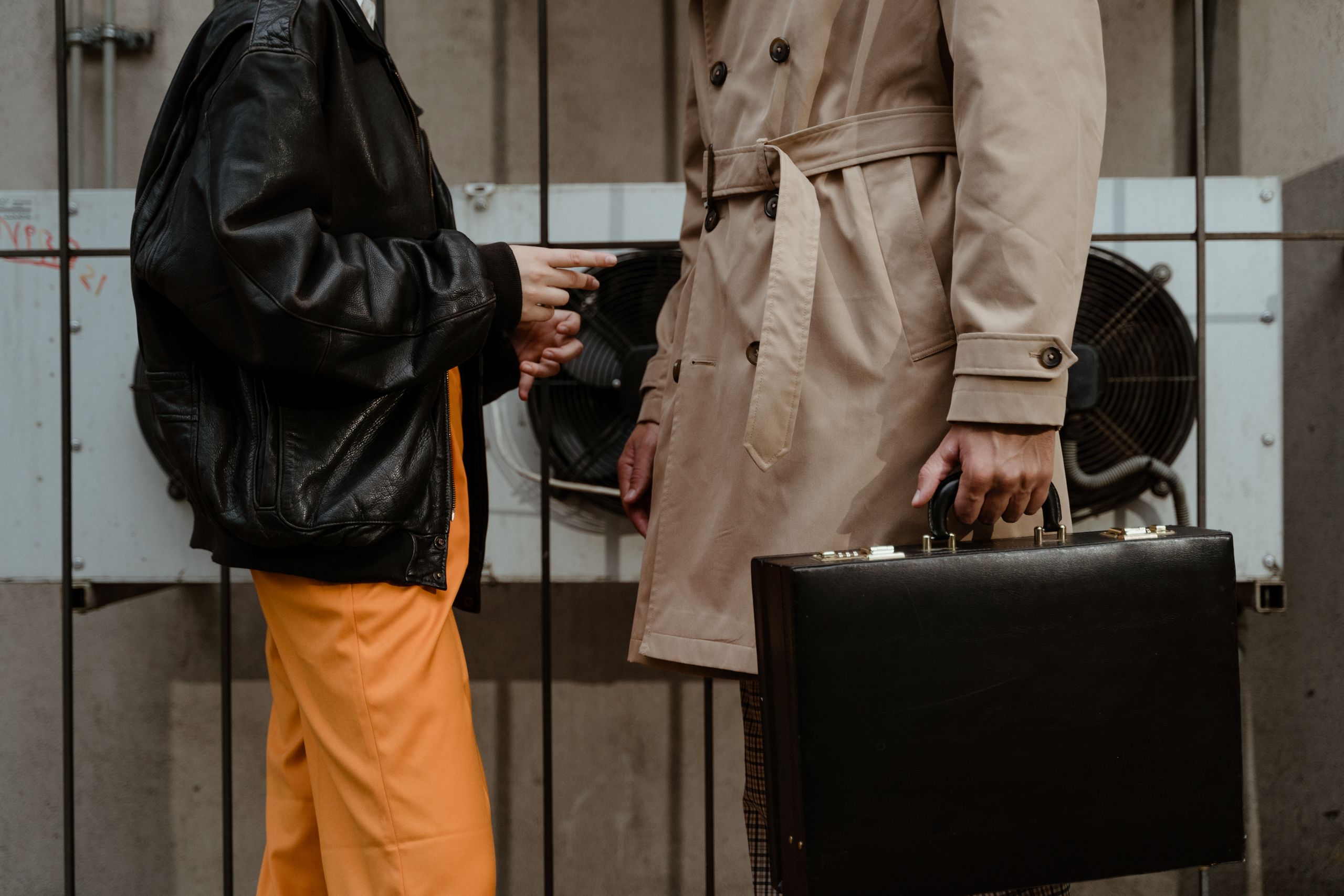 Close-up of two people in an urban setting exchanging a briefcase, creating a mysterious ambiance.