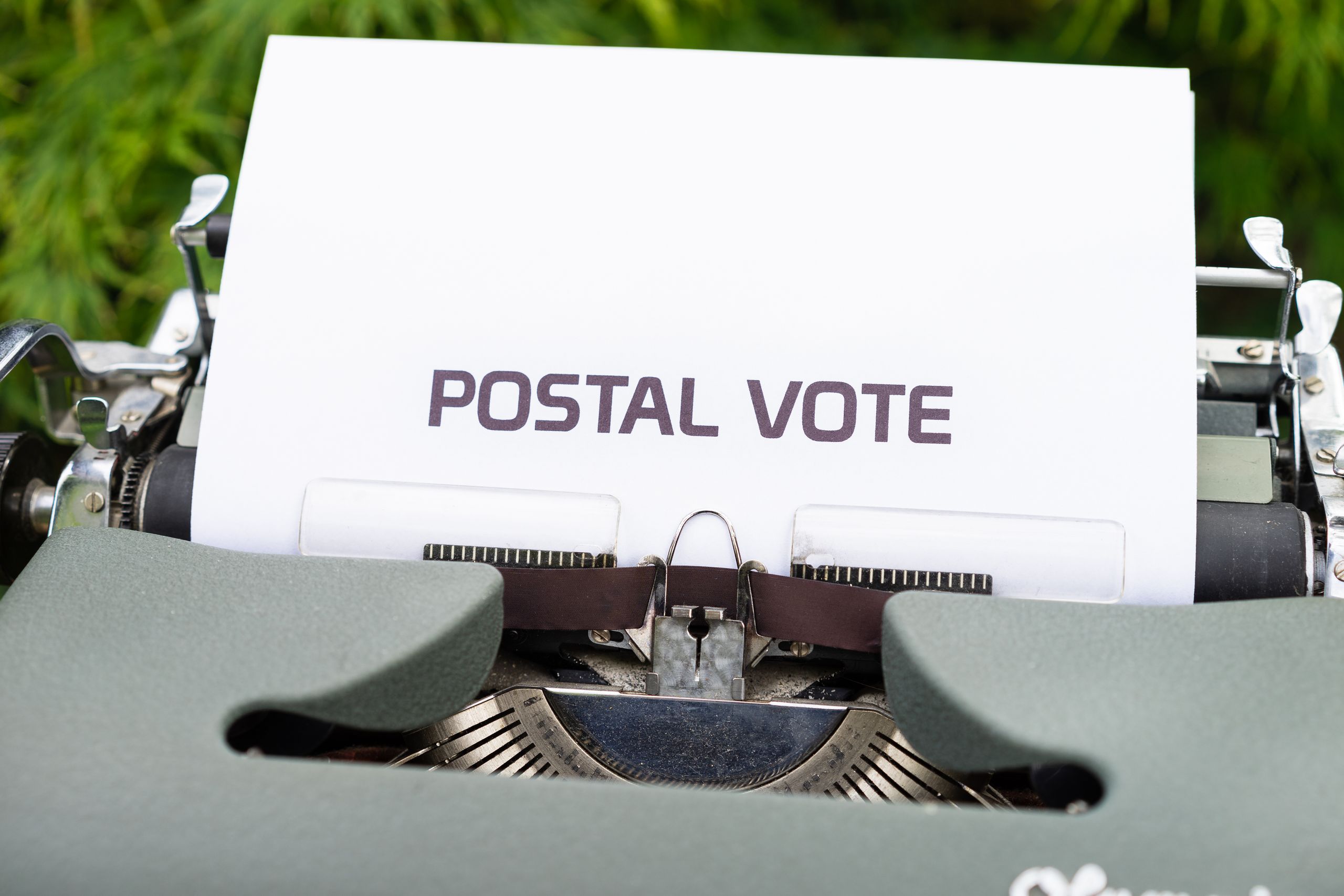 Close-up of typewriter with paper displaying the words 'Postal Vote', outdoors.