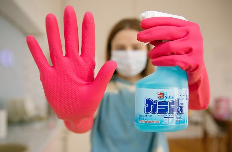Close-up of woman in rubber gloves holding glass cleaner, illustrating housework and hygiene.