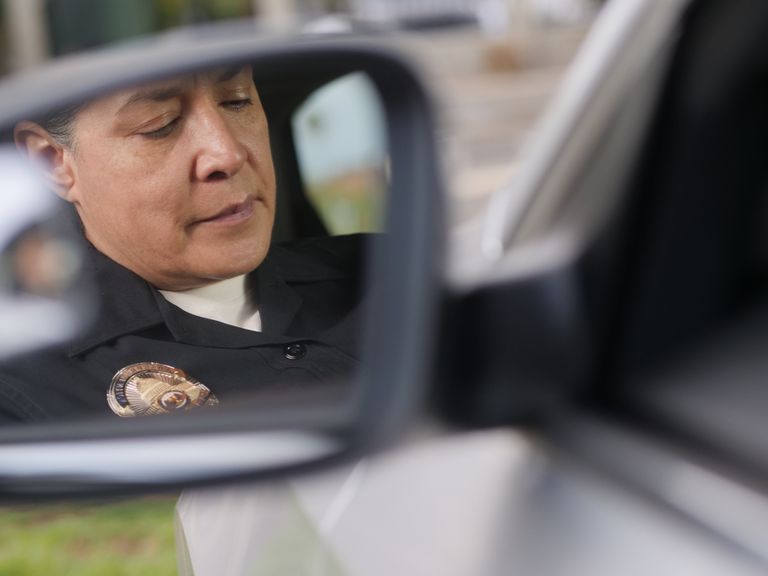 Close-up reflection of a focused police officer in a car side mirror, showcasing authority and vigilance.