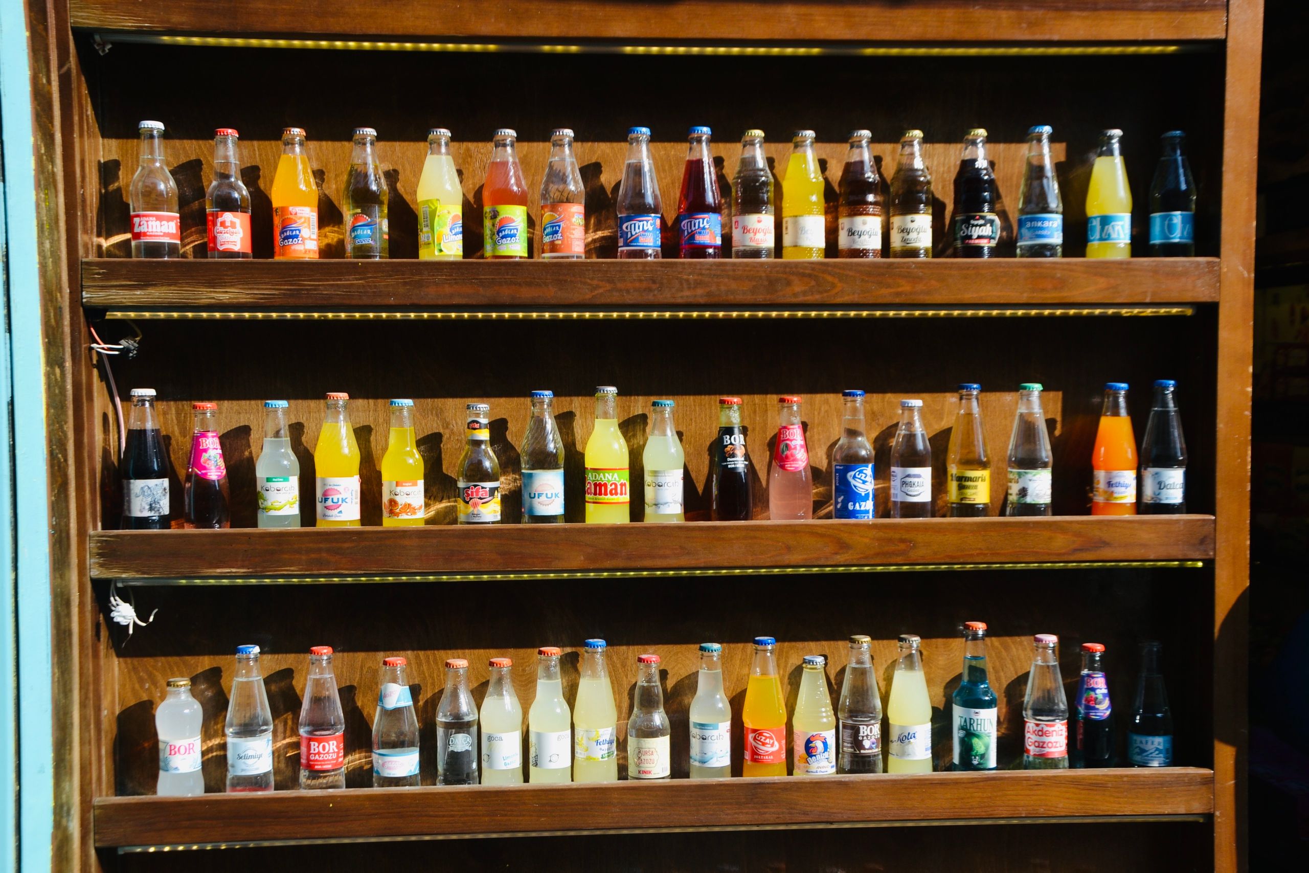 Colorful assortment of soda bottles displayed on wooden shelves in a store setting.