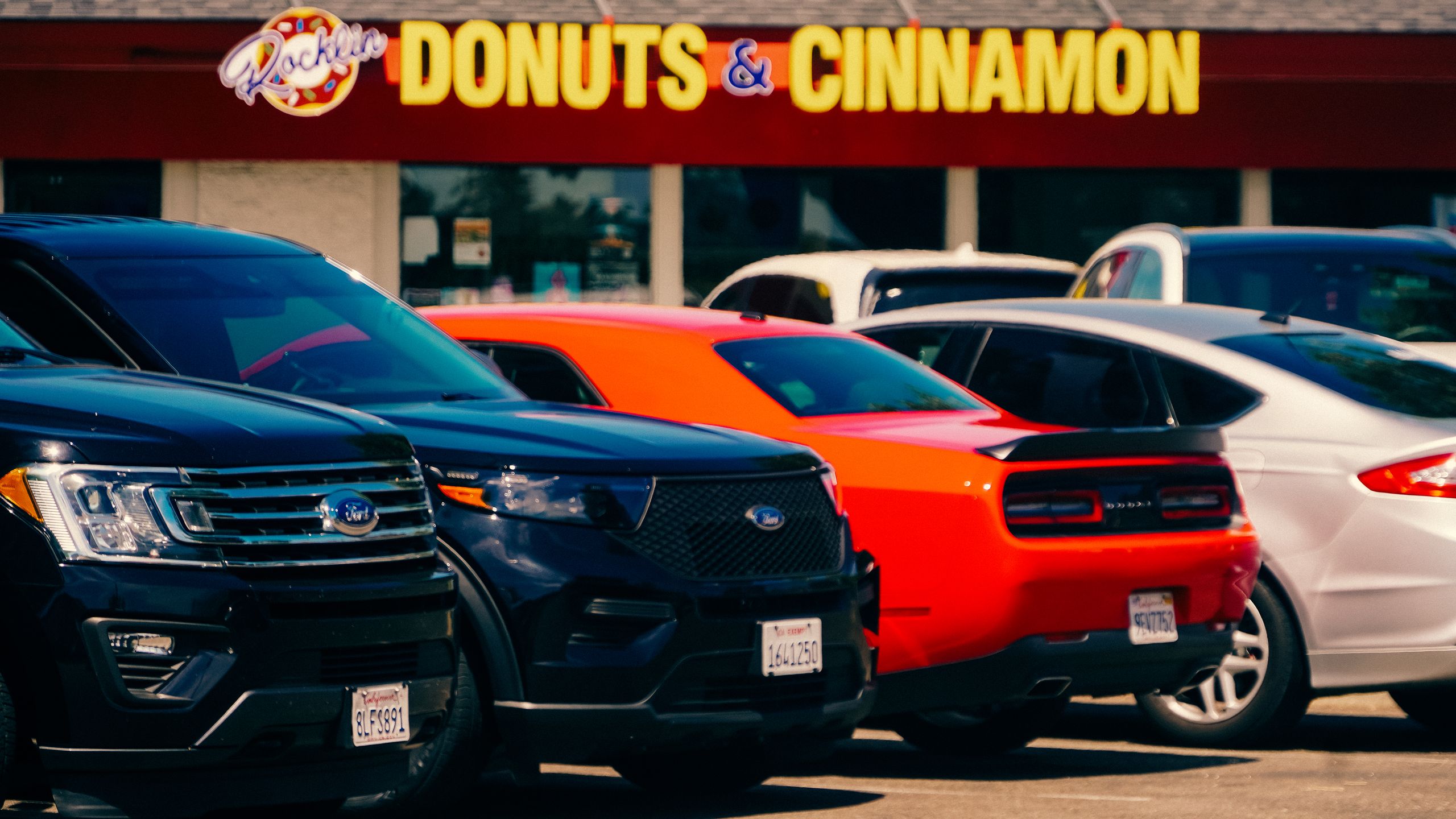 Colorful cars are parked outside a Donut & Cinnamon shop in California, USA.