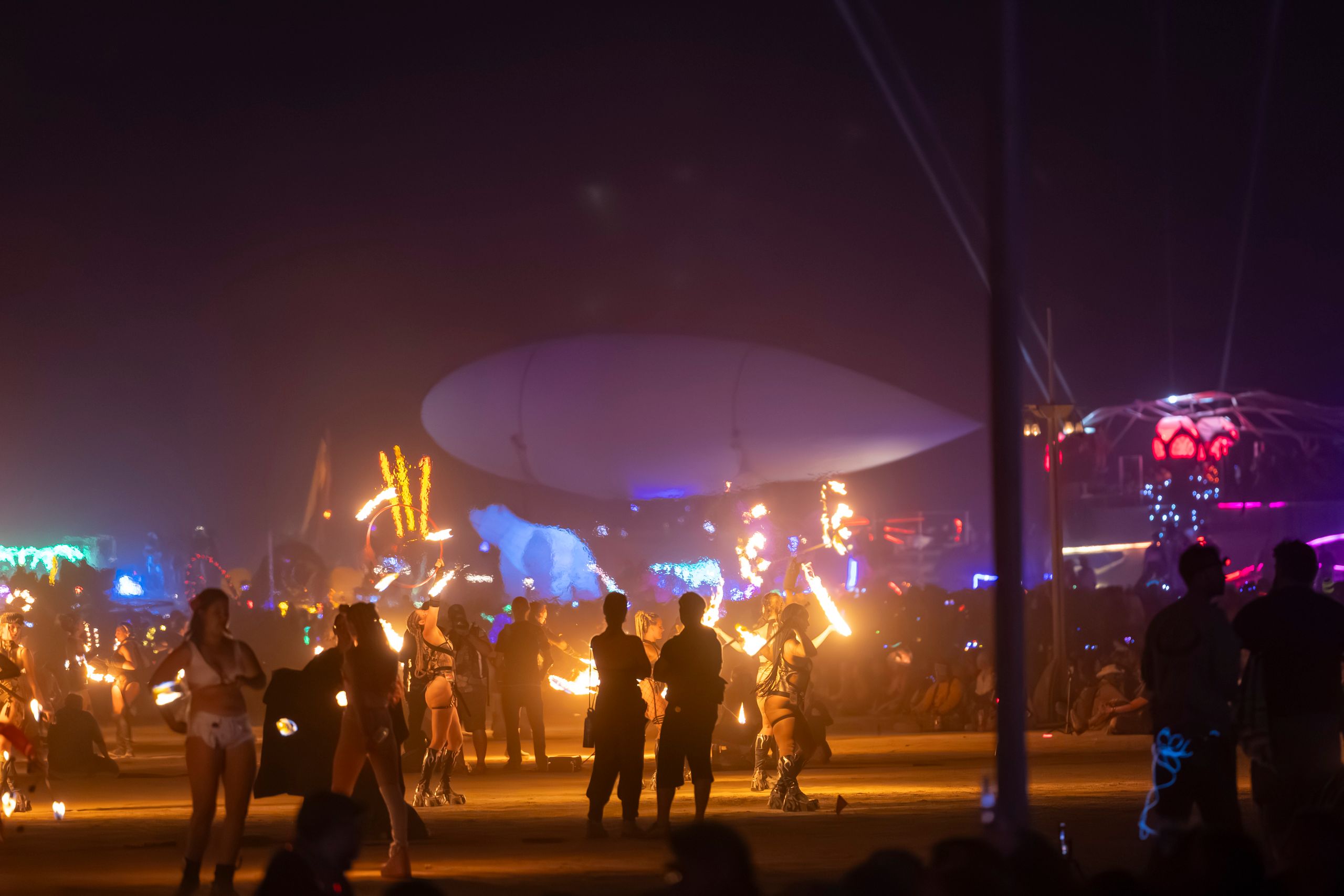 Colorful night scene of fire performers entertaining a crowd at a lively outdoor festival.