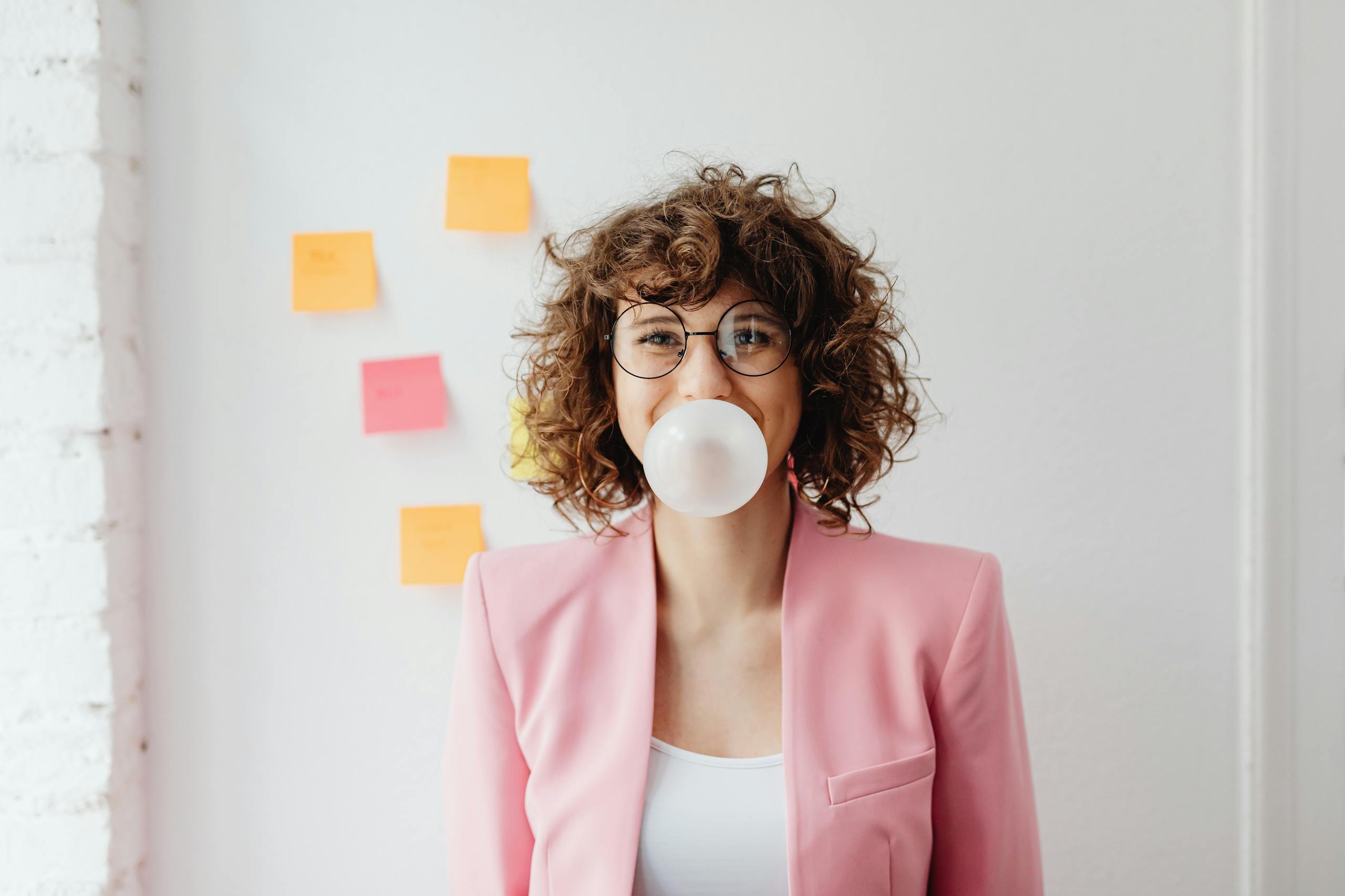 Confident businesswoman with curly hair blowing bubble gum indoors.