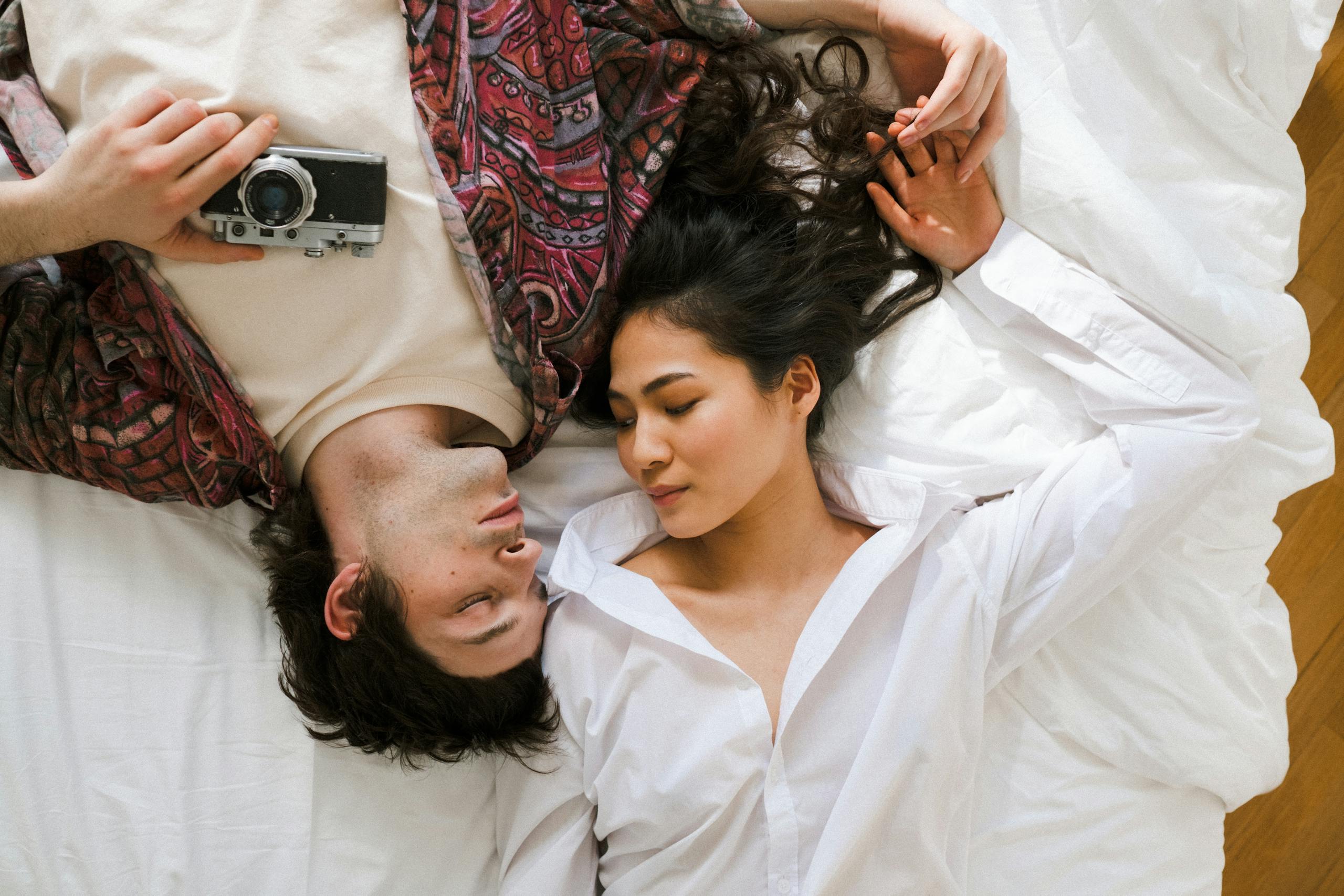 Couple lying together on a bed with a vintage camera. Intimate and serene moment.