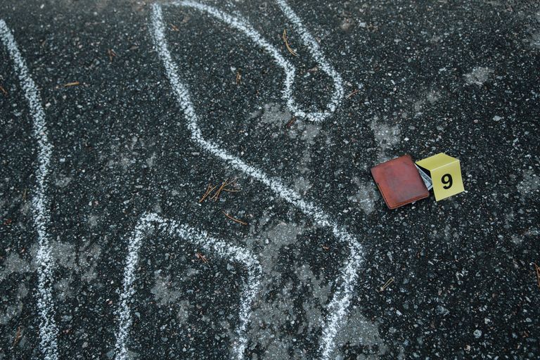 Crime scene with a chalk outline and evidence marker on asphalt.